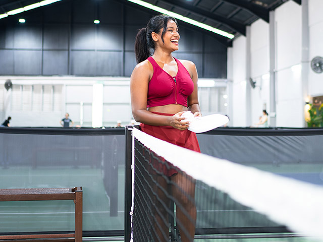 Energetic indoor pickleball match with a smiling player in a vibrant red sports outfit, capturing the excitement and energy of the game.