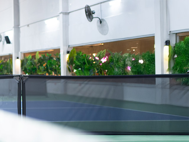 Covered pickleball court with lush greenery and modern lighting, offering a vibrant and inviting sports environment.