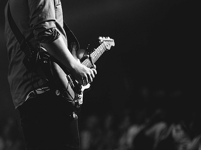 Dynamic black and white photo of a musician passionately playing an electric guitar on stage, capturing the essence of live performance.