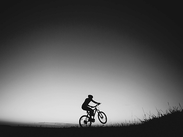 Dynamic silhouette of a cyclist riding uphill at sunset, capturing the thrill of outdoor adventure.