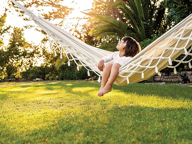 Peaceful backyard escape with a child relaxing on a hammock under the golden sunlight, surrounded by lush greenery.