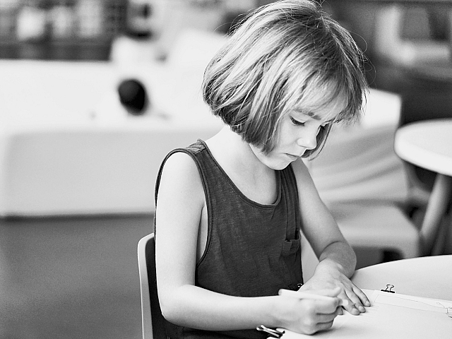 Black and white photo of a young child focused on drawing at a table, highlighting creativity and concentration.