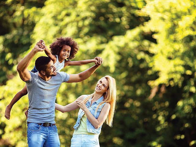 Joyful family enjoying a sunny day outdoors, surrounded by lush green trees.