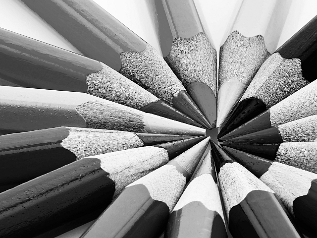 Dynamic black and white photo of colored pencils arranged in a vibrant radial pattern.