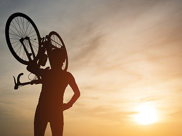 Silhouette of a cyclist lifting their bike triumphantly against a vibrant sunset sky.