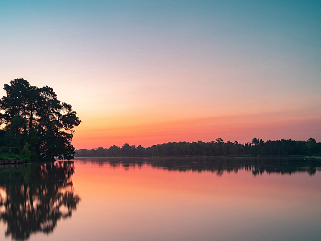 Serene lakeside view with vibrant sunset hues and lush trees reflecting on the tranquil water.