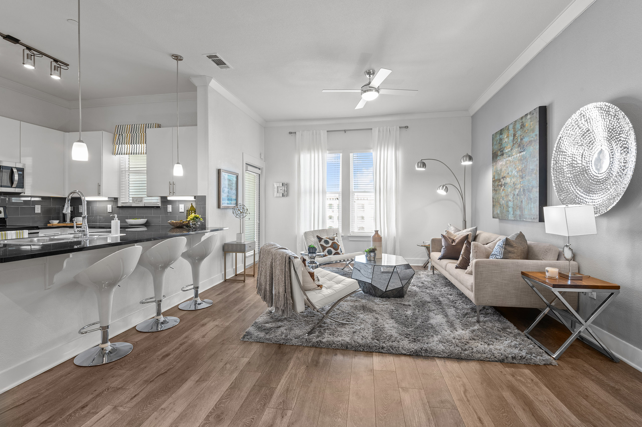 Modern apartment interior with an open-concept living room and kitchen, featuring sleek bar stools, contemporary lighting, and stylish decor.