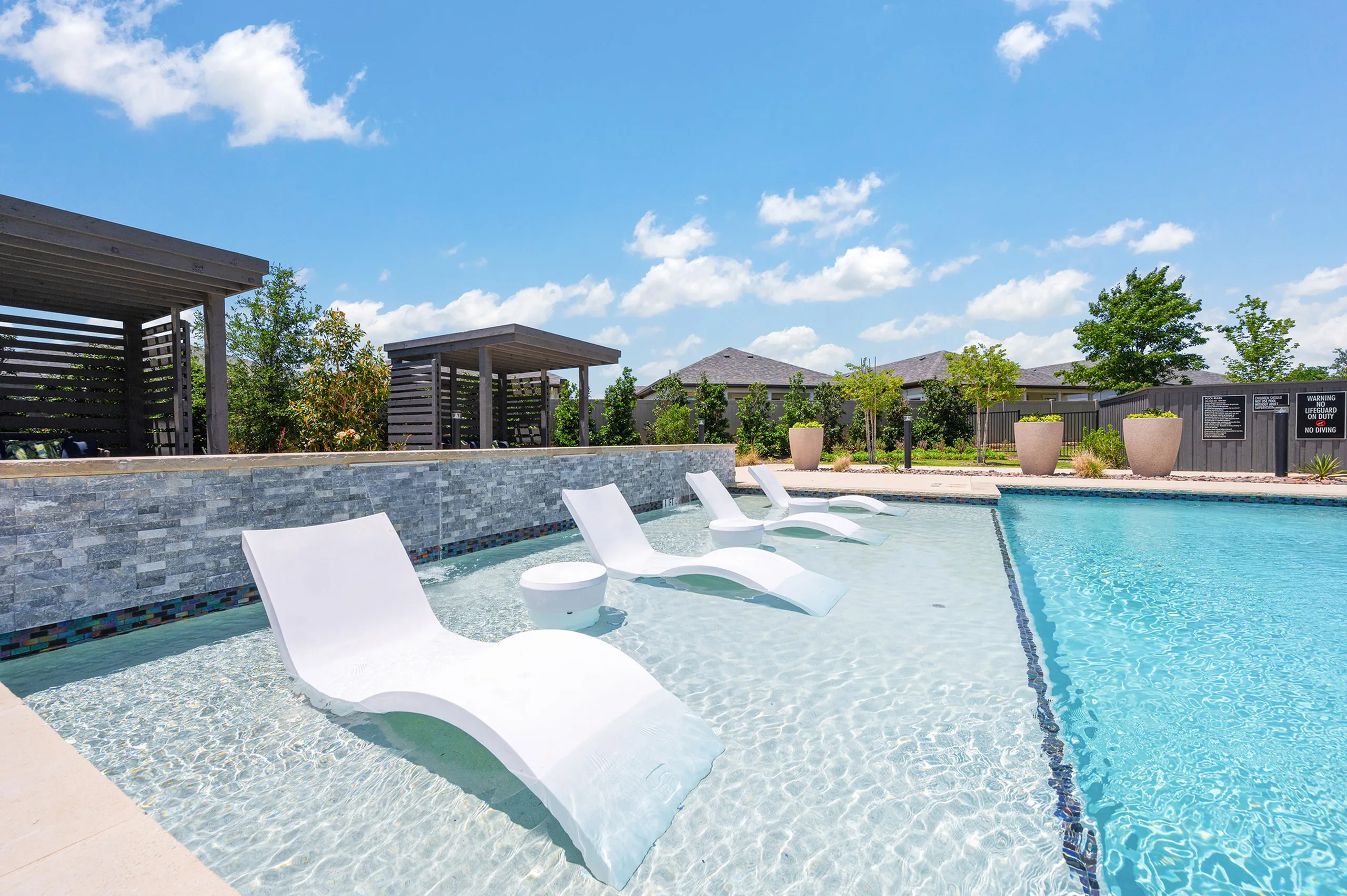 Luxurious outdoor swimming pool with loungers and stylish wooden cabanas, set under a bright blue sky.