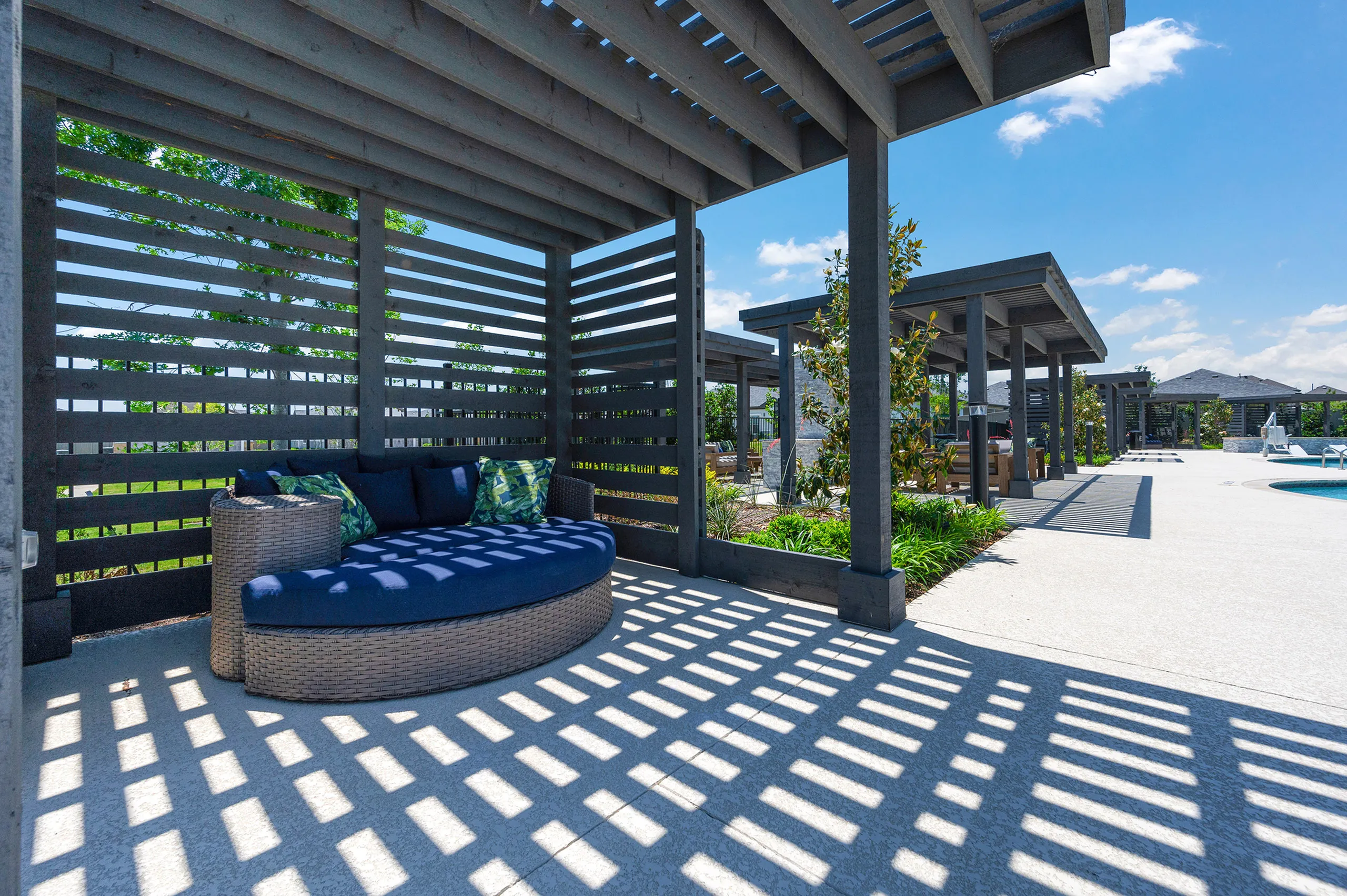 Luxurious outdoor lounge with modern pergolas, cushioned seating, and a bright blue sky, perfect for relaxation by the pool.