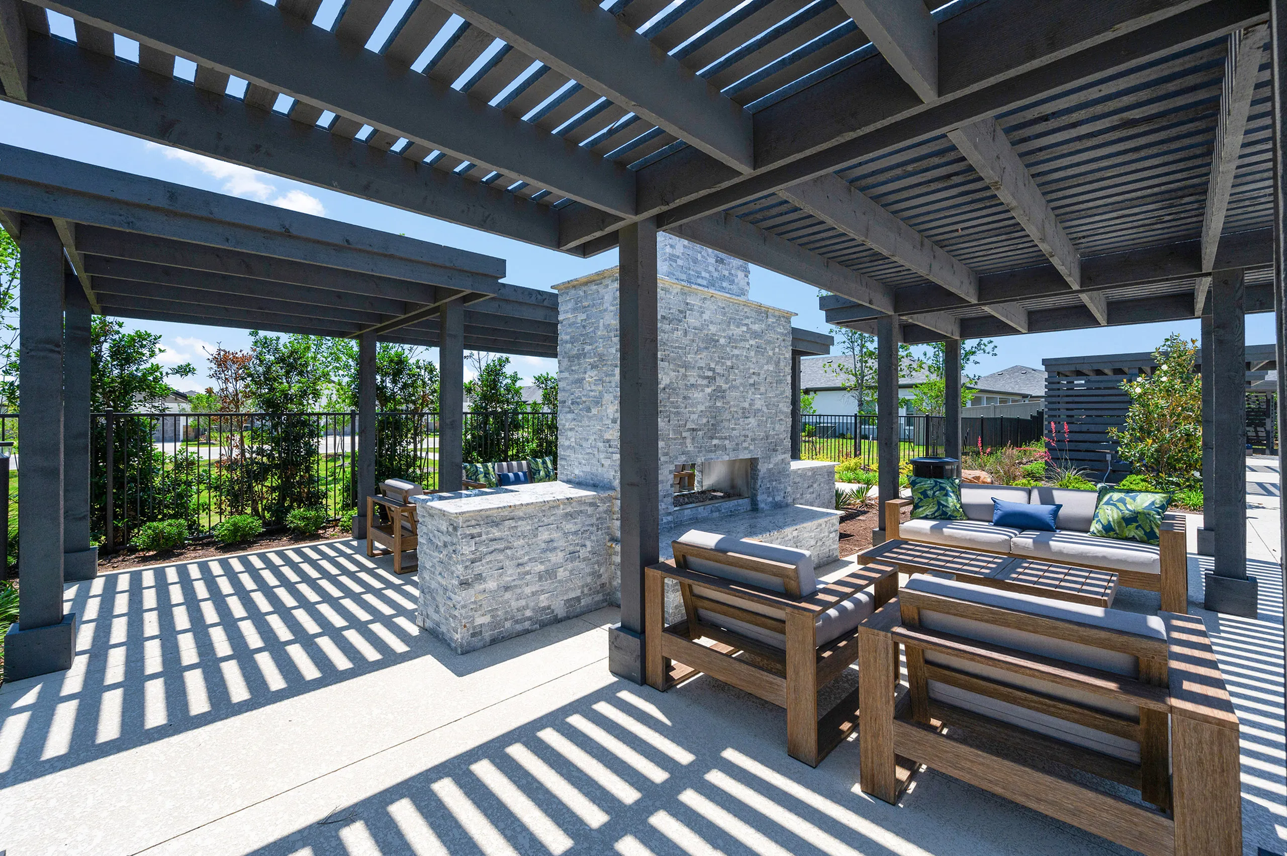 Chic outdoor patio with shaded pergola, modern stone fireplace, and stylish wooden seating, perfect for relaxation and entertainment.