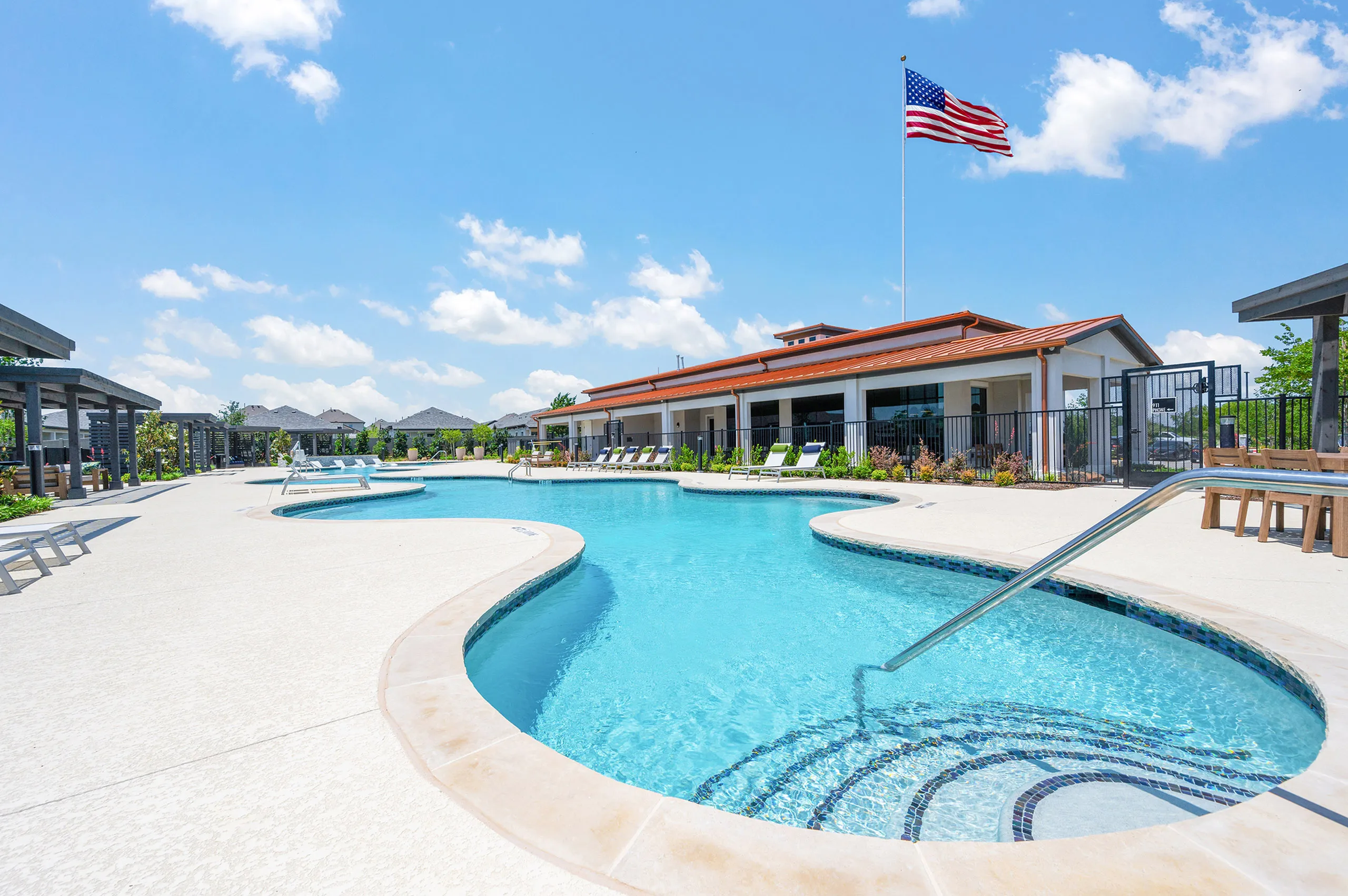 Vibrant apartment complex with inviting swimming pool, sun loungers, and beautiful landscaping under a clear blue sky.