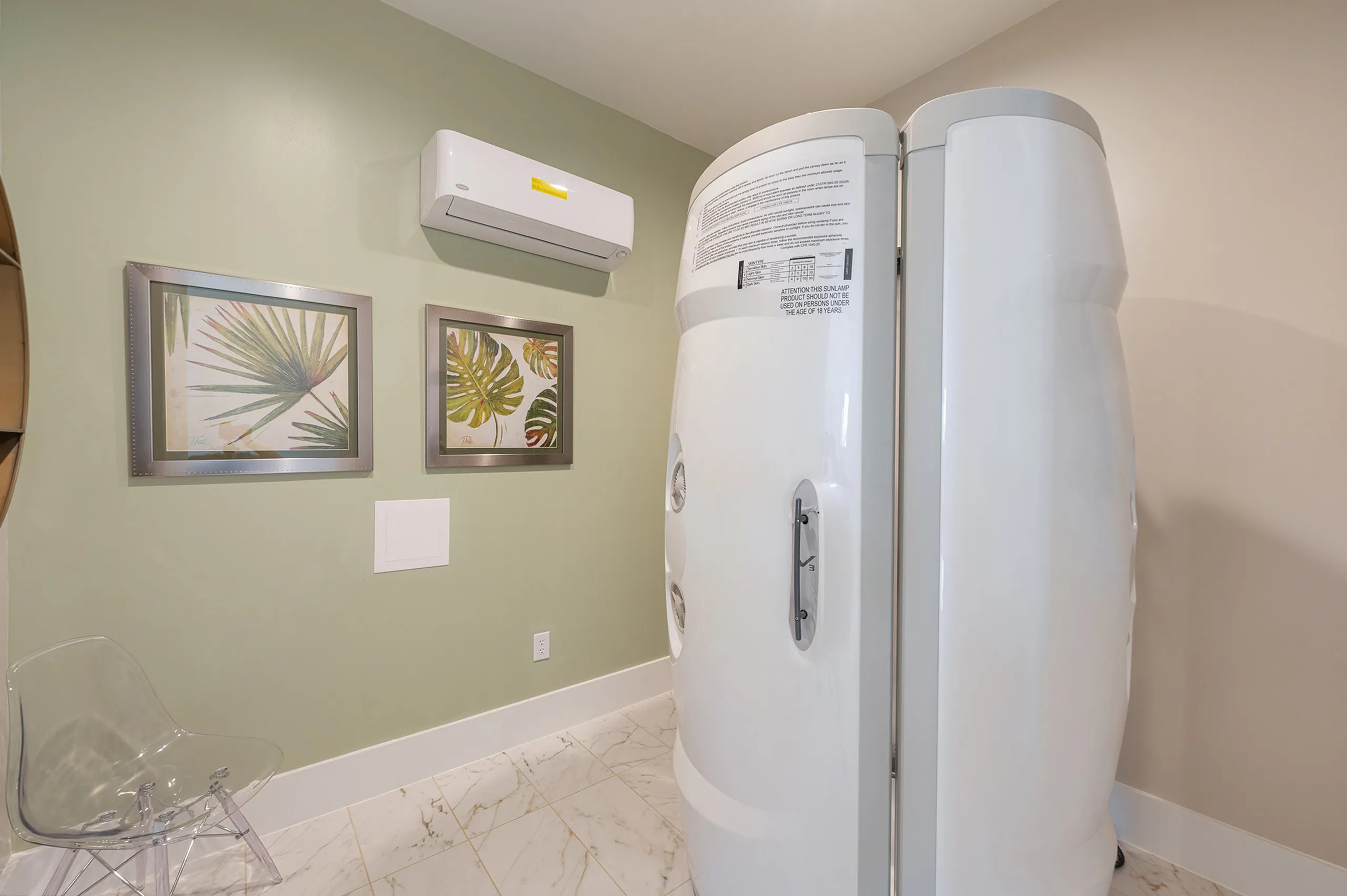Modern wellness room featuring a sleek white cryotherapy chamber, elegant palm leaf artwork, and stylish minimalist decor.