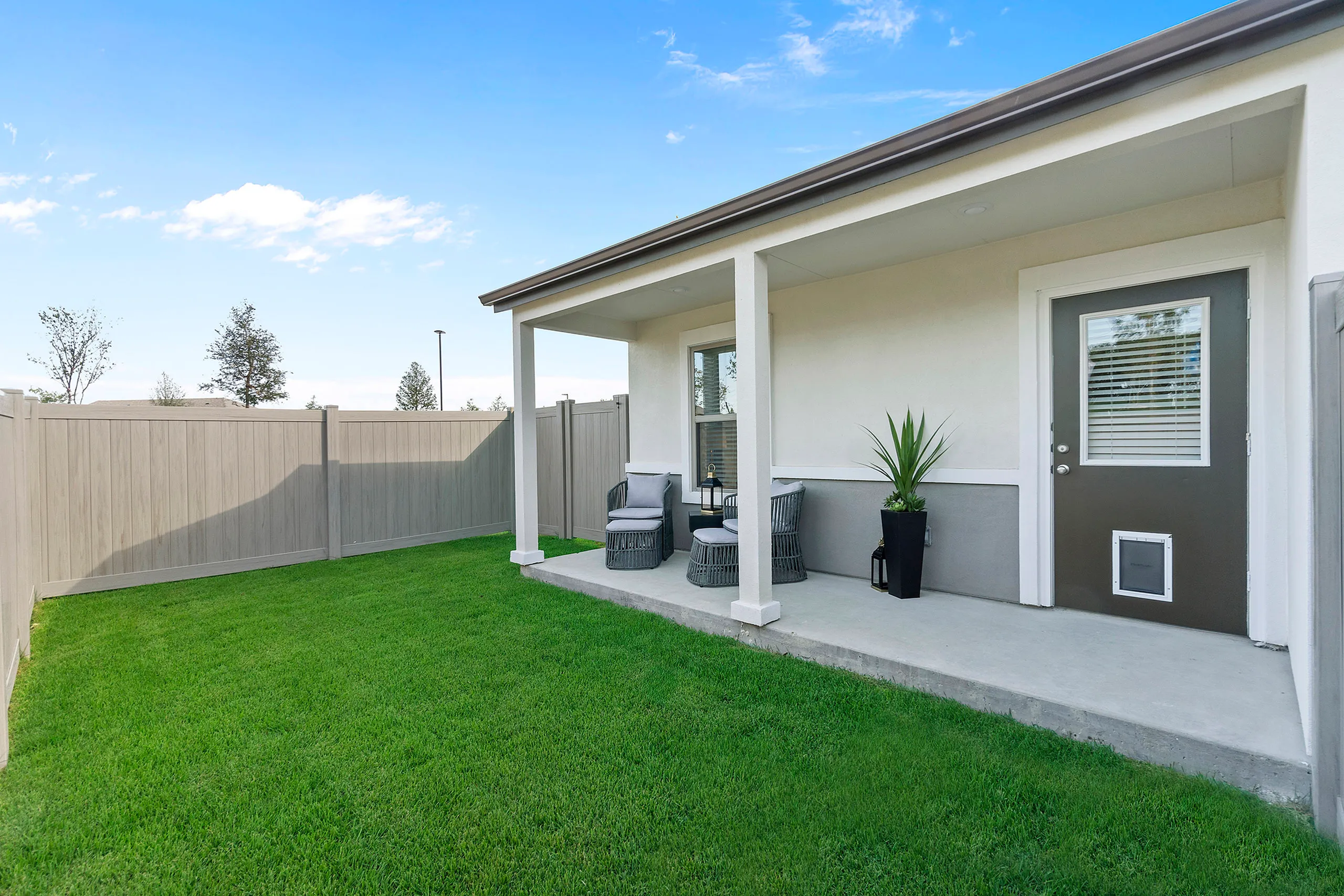 Charming backyard patio with cozy seating, lush green lawn, and modern privacy fence under a clear blue sky.