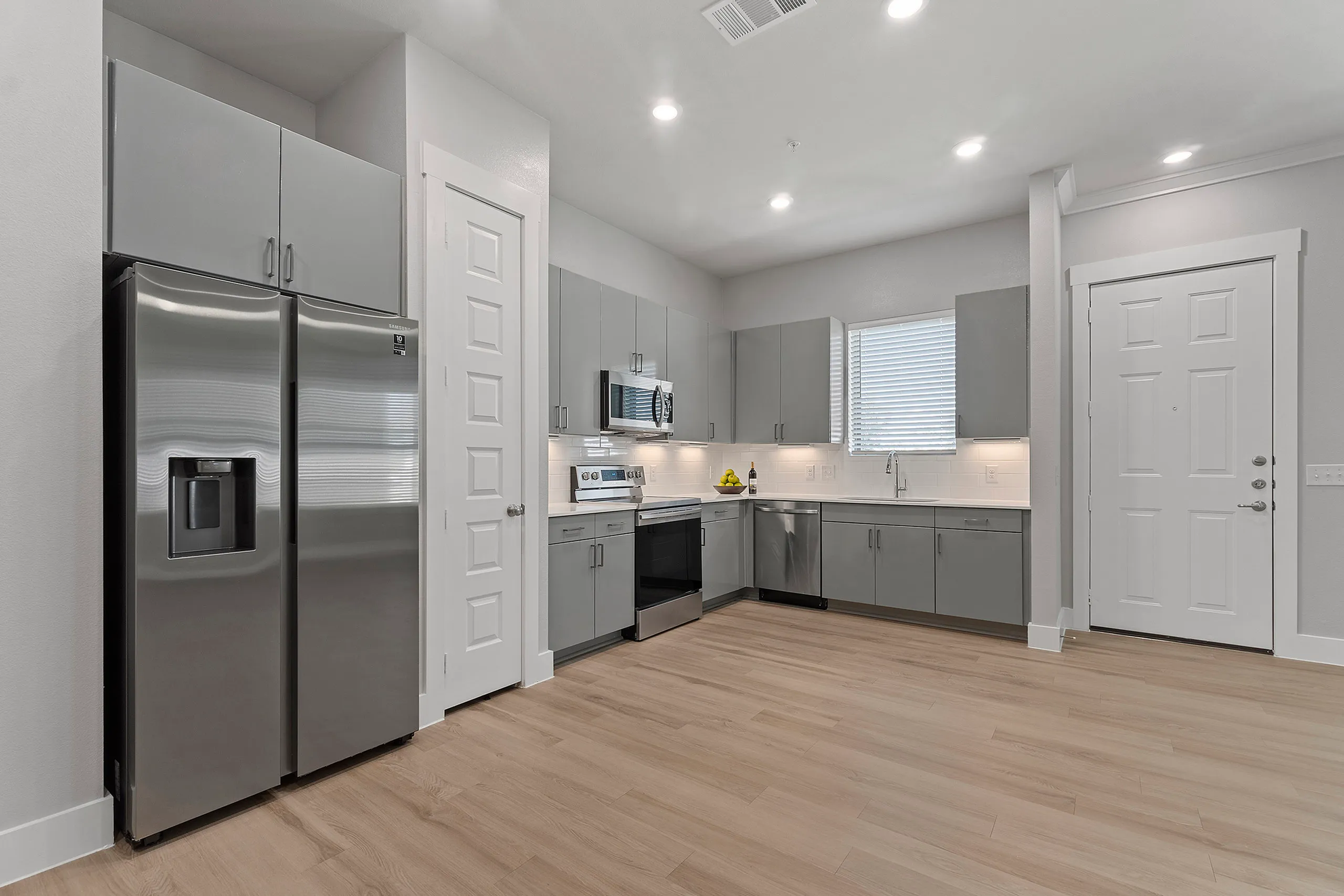 Modern kitchen with sleek gray cabinetry, stainless steel appliances, and light wood flooring, illuminated by recessed lighting.