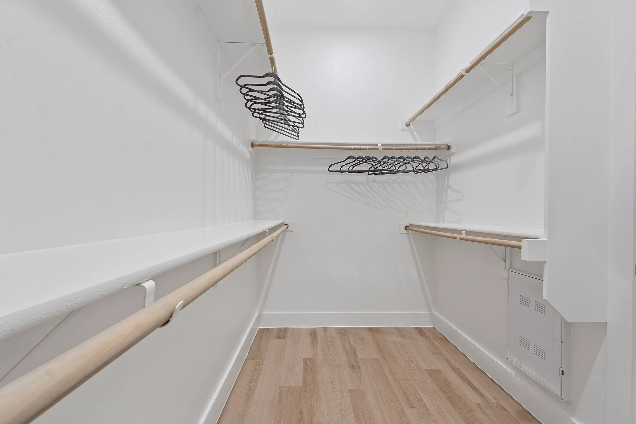 Spacious walk-in closet with elegant wooden floor, ample clothing racks, and modern white walls.