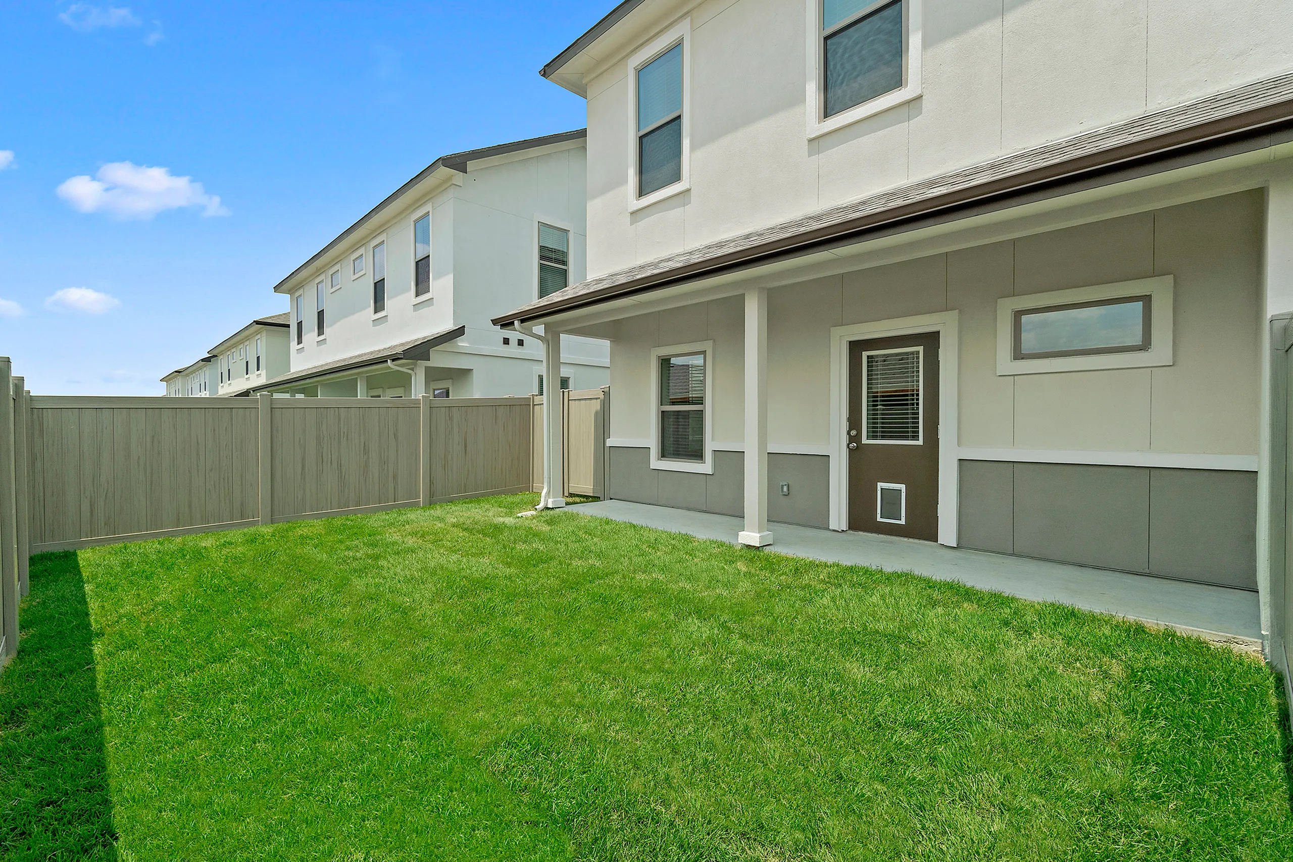 Charming townhouse with a fenced backyard showcasing lush green grass and a cozy patio area.