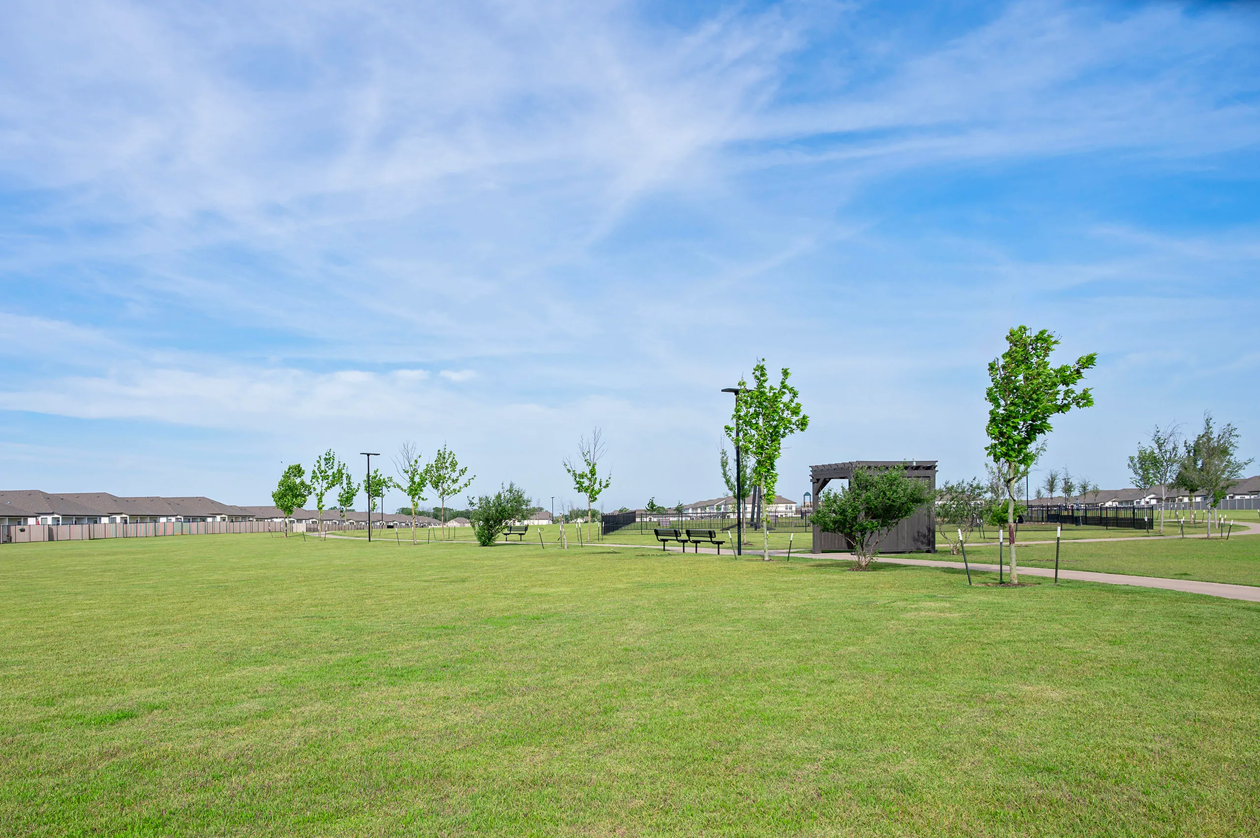 Expansive green outdoor space with a clear blue sky, featuring scattered trees, benches, and a gazebo, perfect for relaxation and community gatherings.