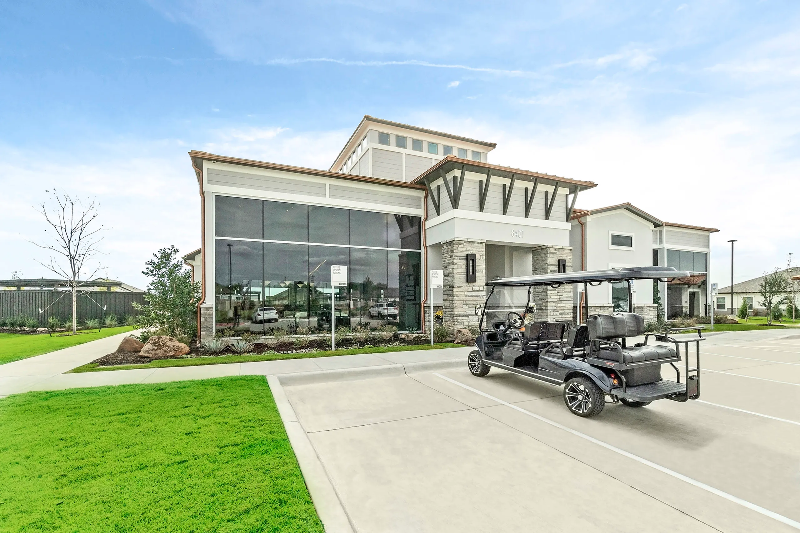 Modern clubhouse with expansive glass windows, stylish landscaping, and a golf cart parked outside, capturing luxury and convenience.