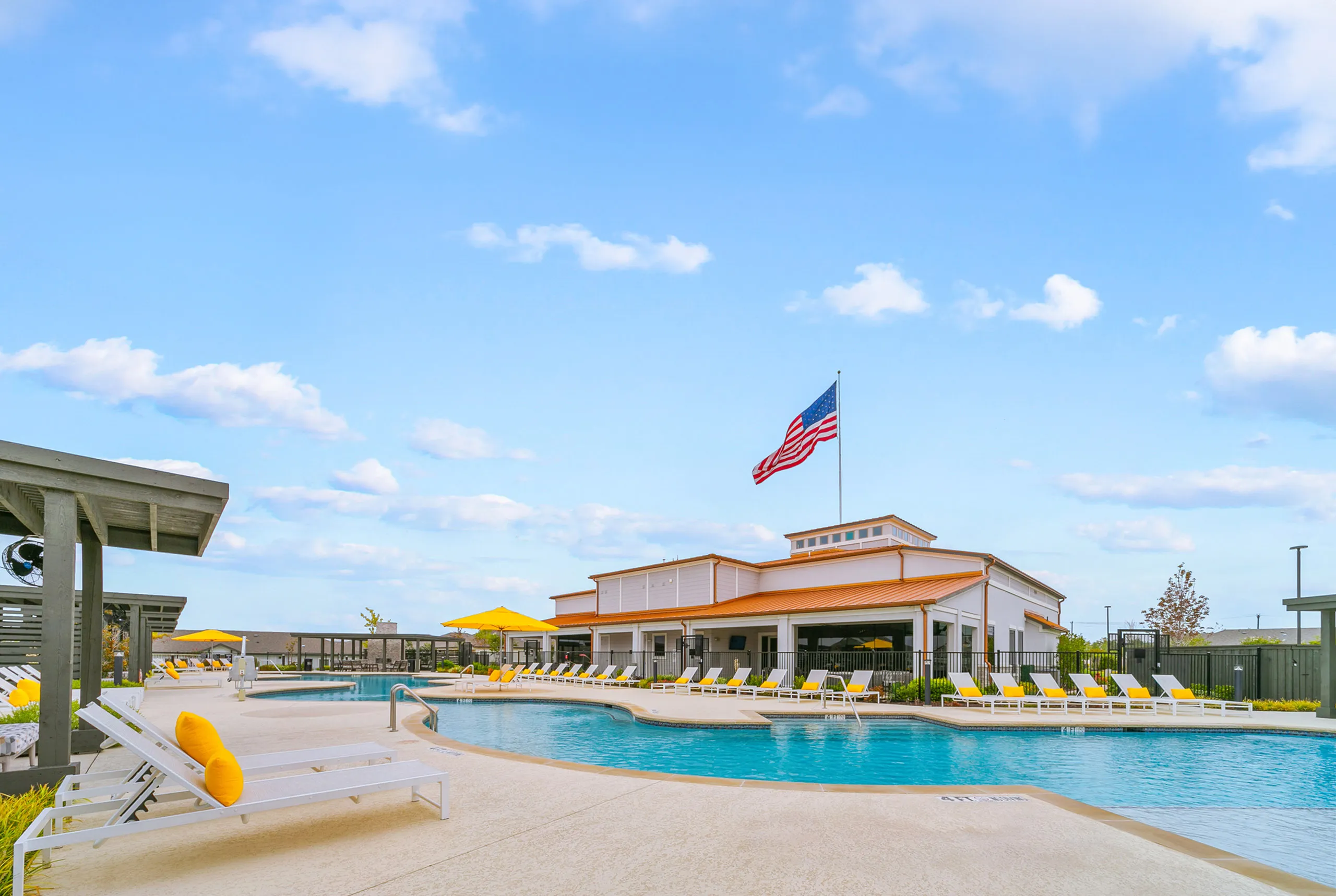 Inviting pool area with vibrant yellow loungers and a clubhouse under a clear blue sky, perfect for relaxation and leisure.