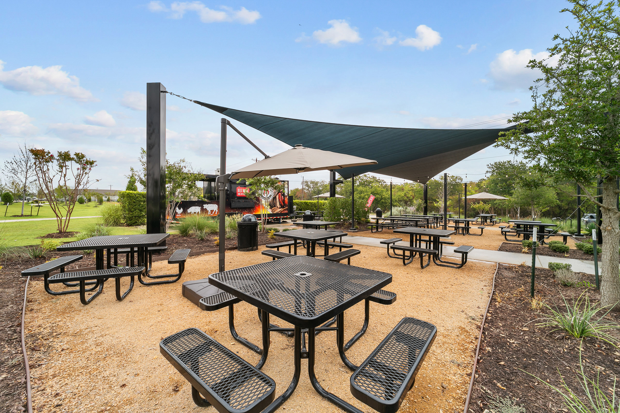 Inviting outdoor picnic area with modern shade sails, surrounded by lush greenery and spacious seating.