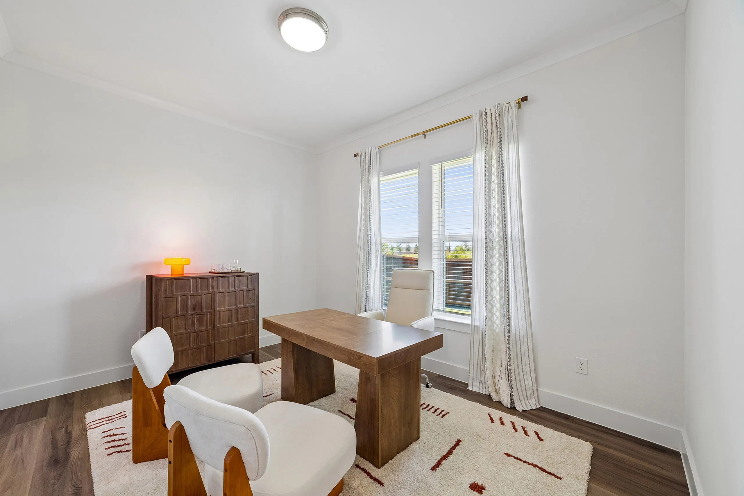 Bright and inviting home office with large windows, modern wooden desk, and stylish chairs, bathed in natural light.