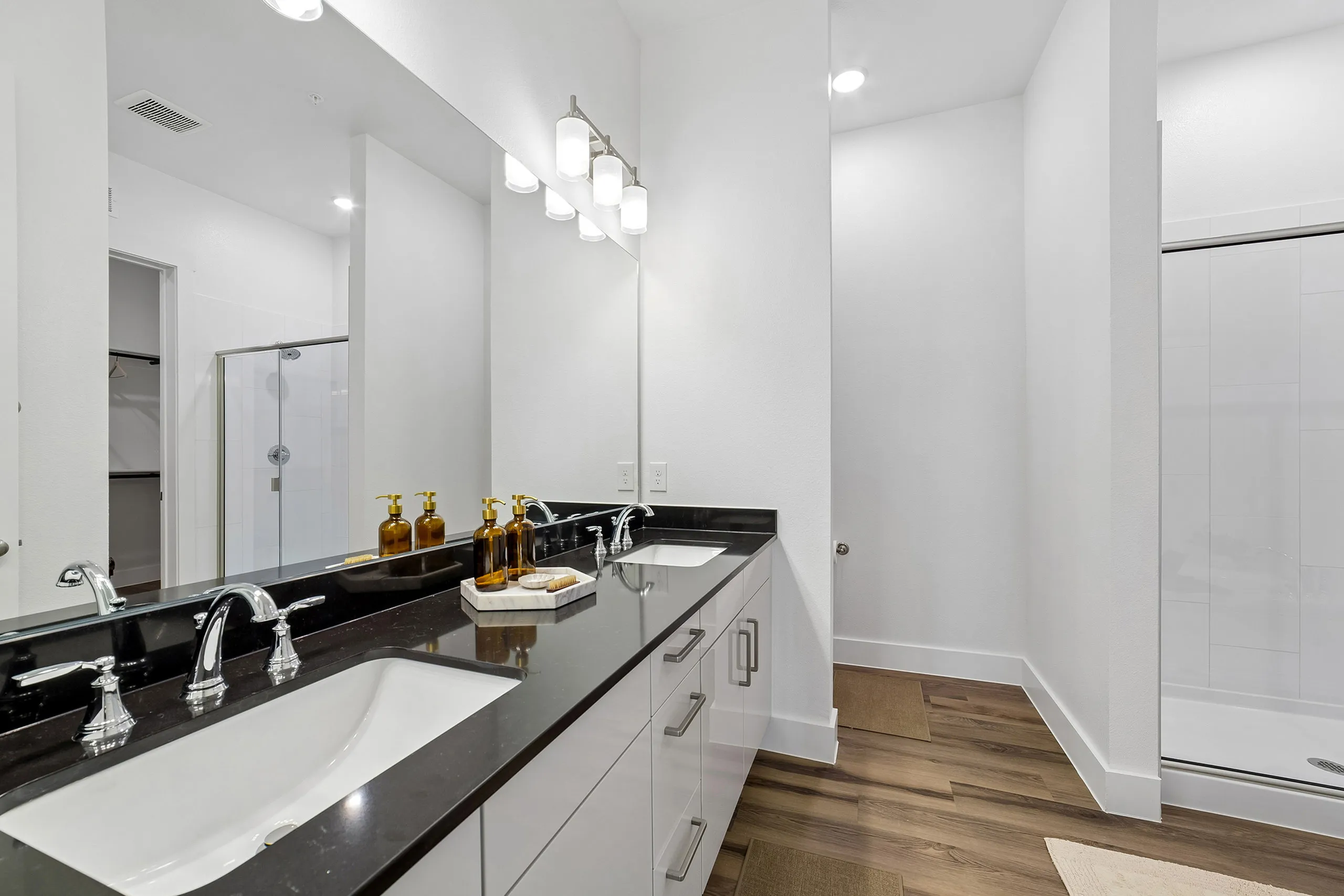 Elegant bathroom with dual sinks, sleek black countertops, and a spacious walk-in shower, offering a blend of style and functionality.