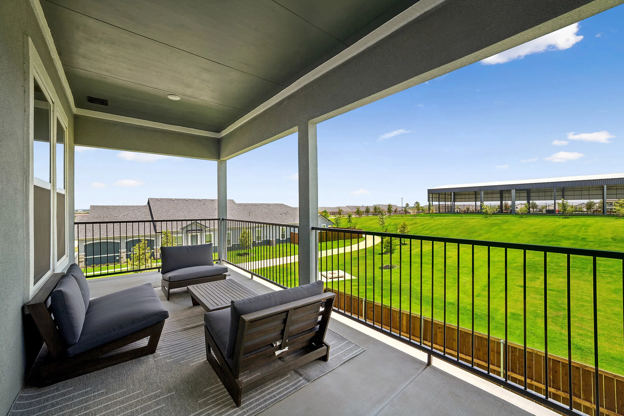 Elegant balcony with cozy seating overlooking lush green lawn and modern architecture under a clear blue sky.