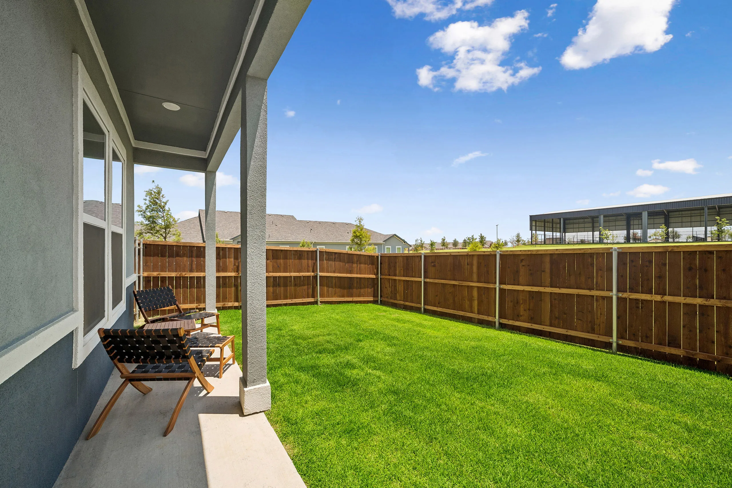 Charming patio space with comfortable chairs overlooking a lush green backyard and wooden fence under a sunny blue sky.