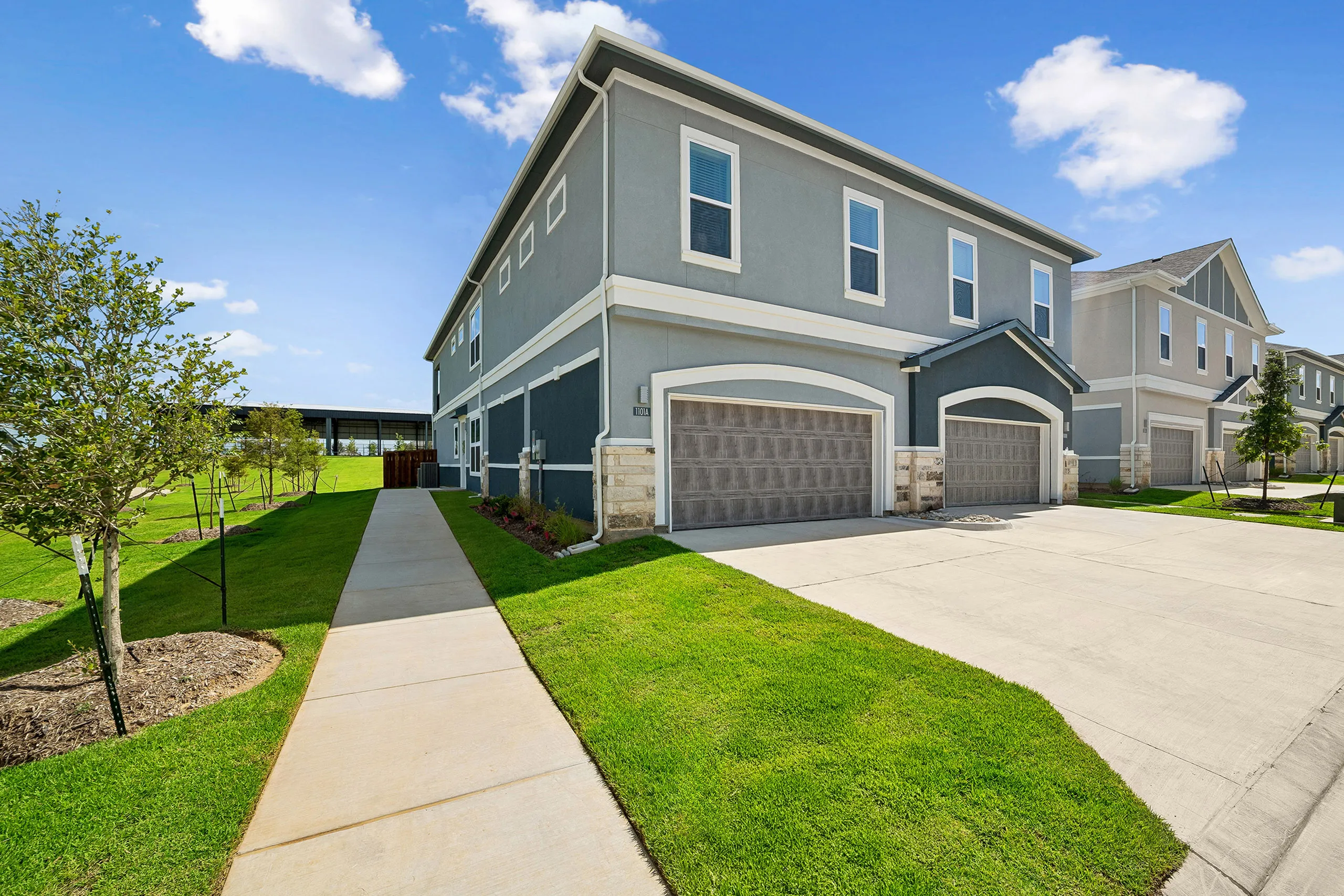 Modern townhouse exterior with a charming two-story design, featuring immaculate landscaping, a spacious driveway, and bright, inviting façades against a clear blue sky.