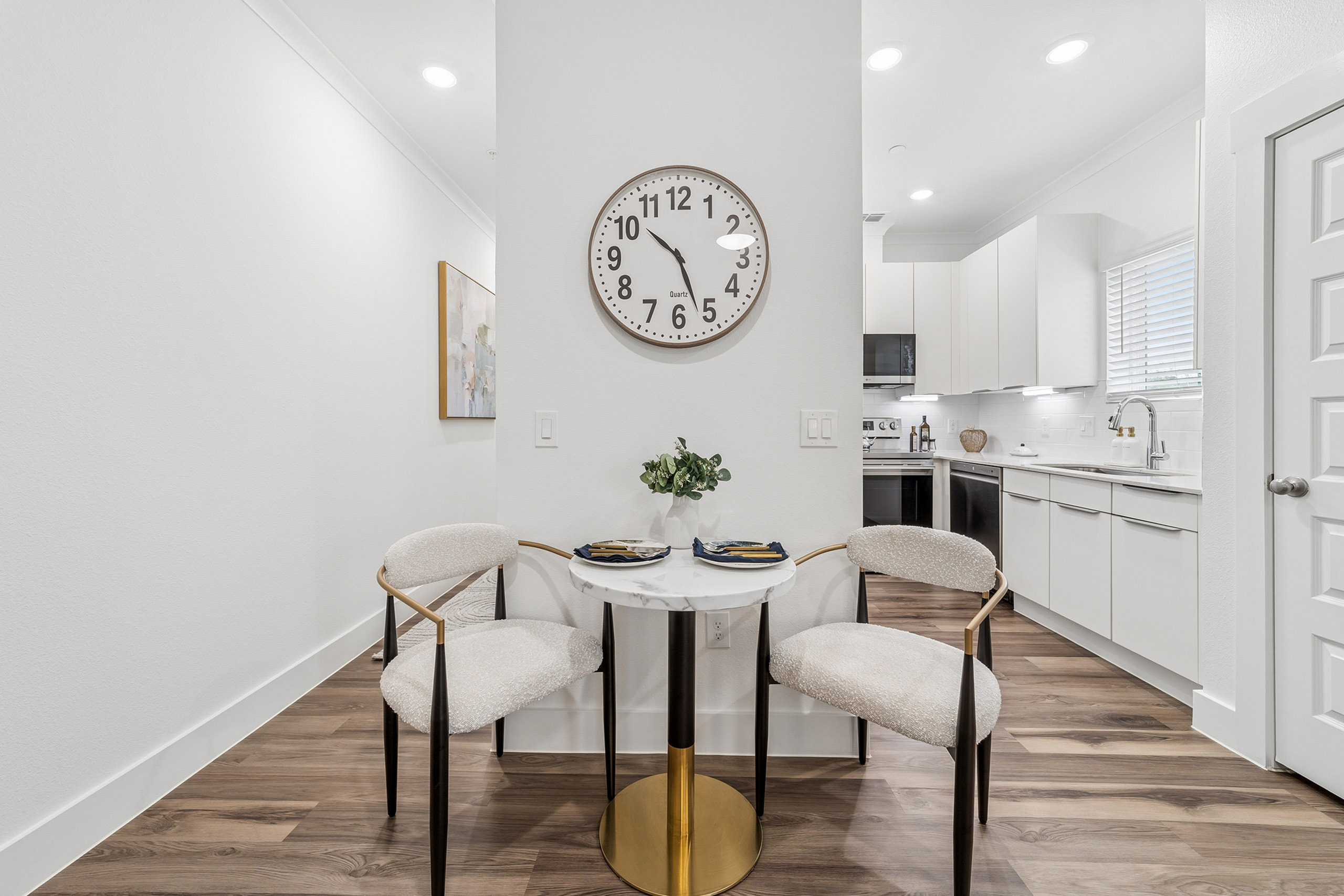 Chic dining nook with a round marble table and elegant chairs, adjacent to a modern, bright kitchen with sleek cabinetry and hardwood flooring.
