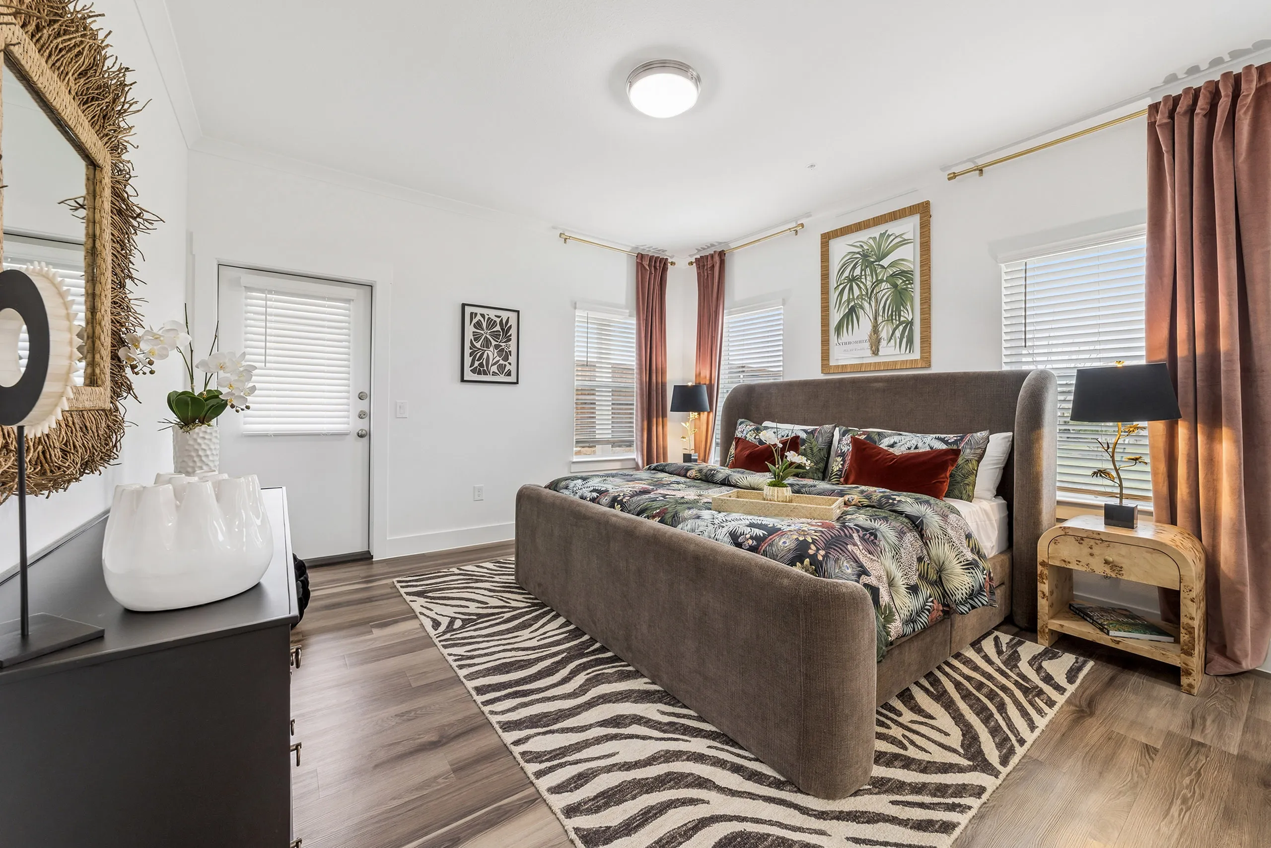 Elegant bedroom with modern decor featuring a plush bed, vibrant pillows, zebra-print rug, and abundant natural light from large windows.