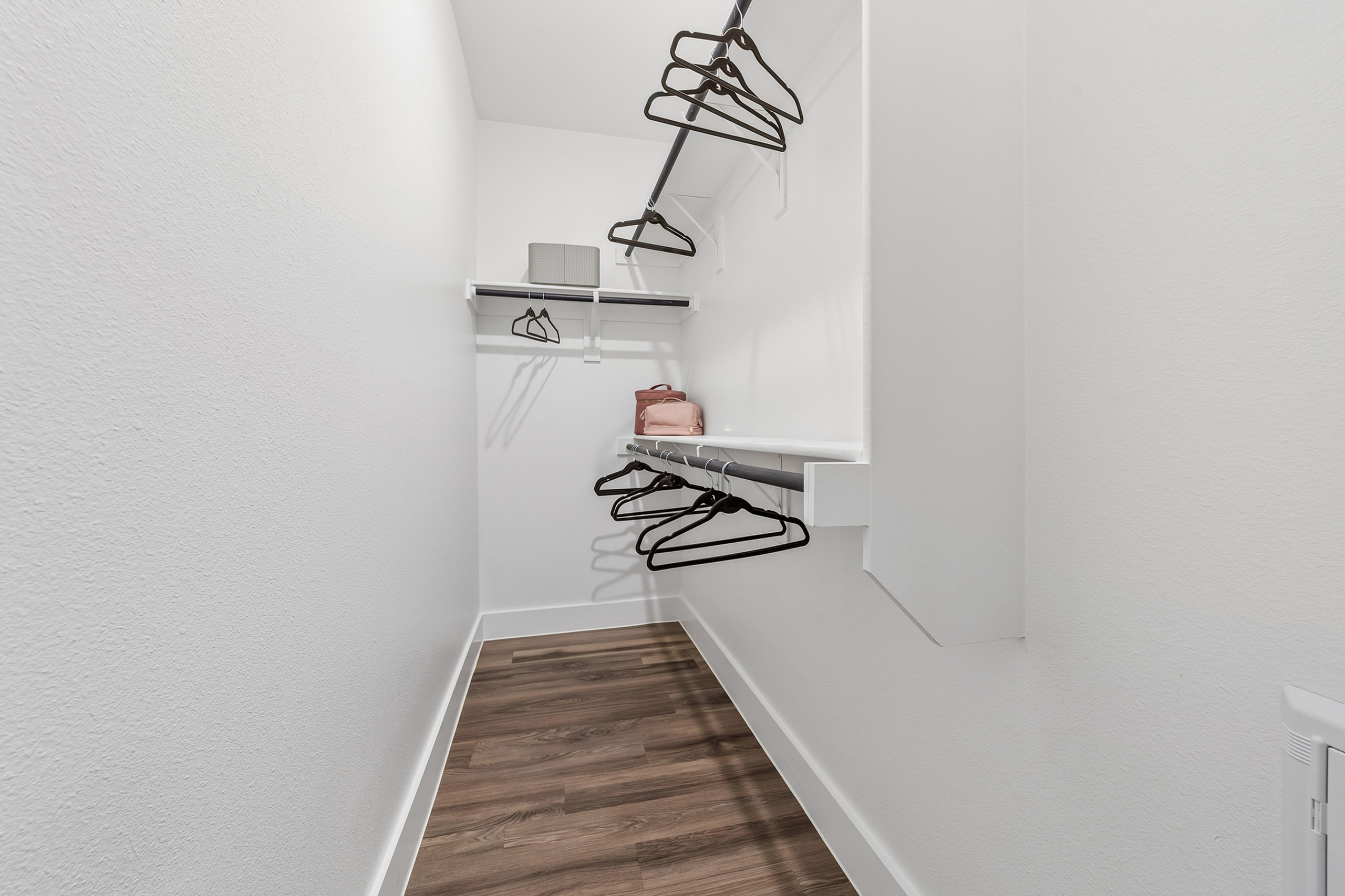 Spacious walk-in closet with sleek wooden flooring, outfitted with ample shelving and modern hanger rods.