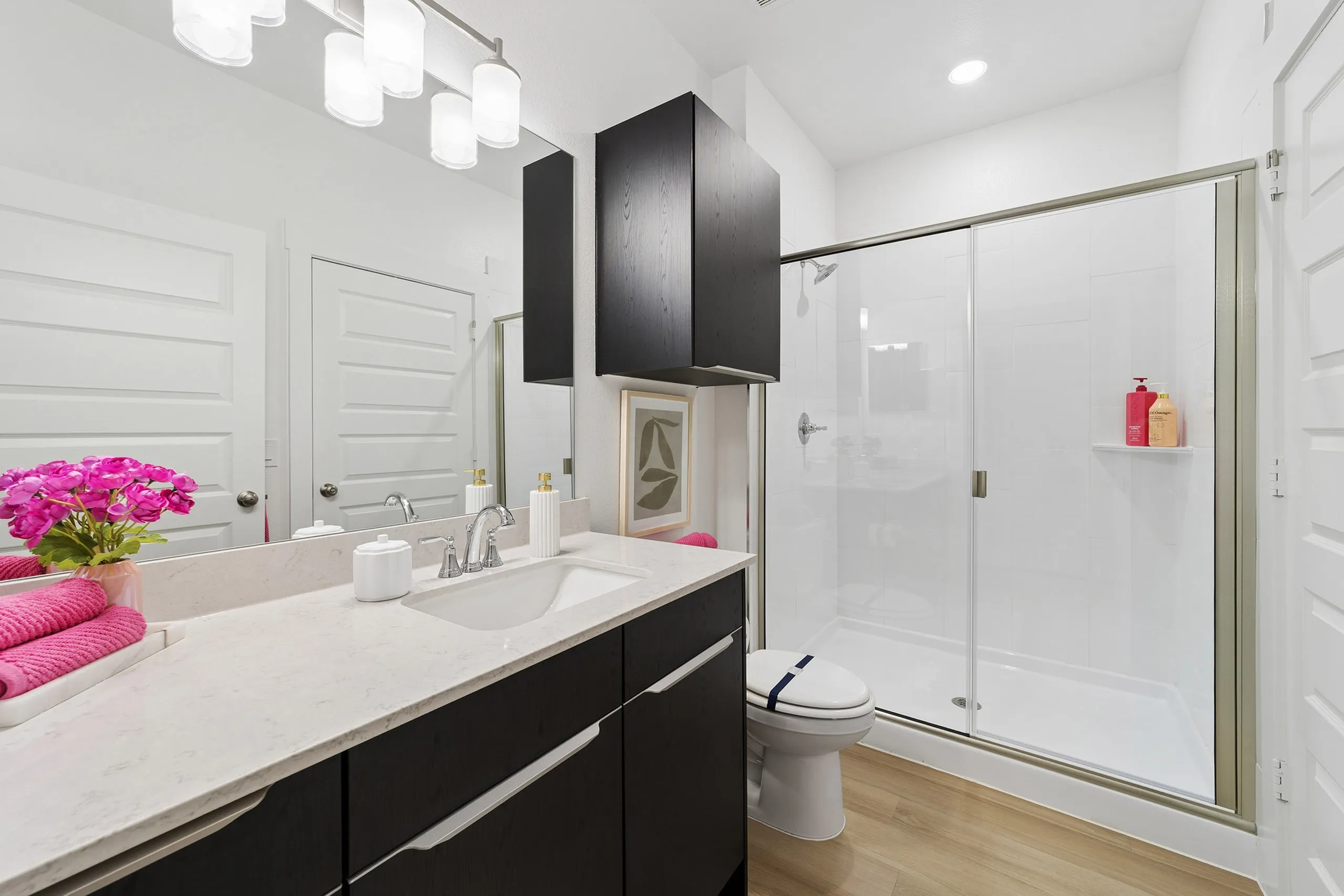 Modern bathroom with sleek black cabinet, elegant glass shower, and stylish vanity featuring vibrant flowers and contemporary decor.