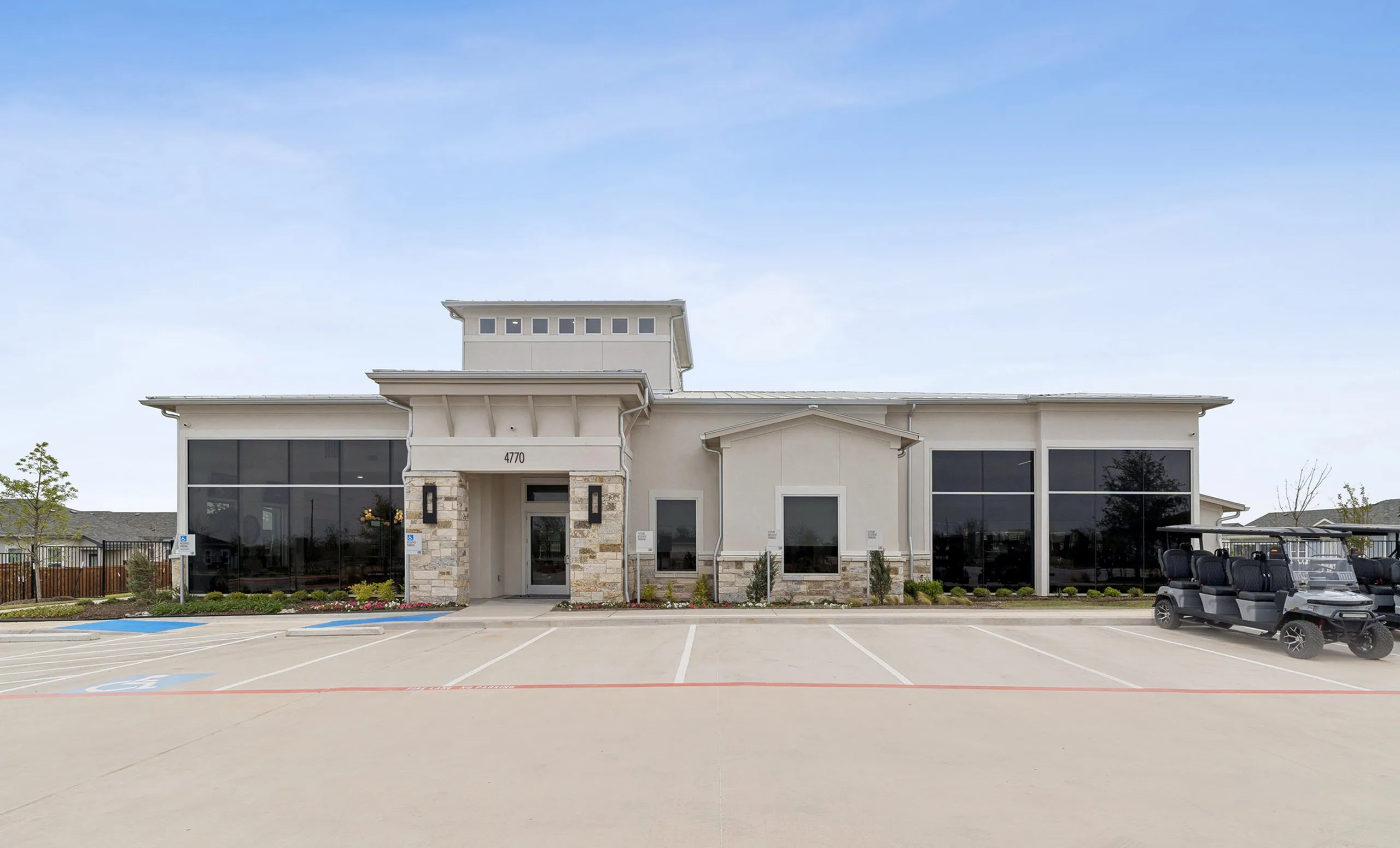 Modern apartment building with large windows and clean architectural design, offering ample parking and a welcoming entrance.