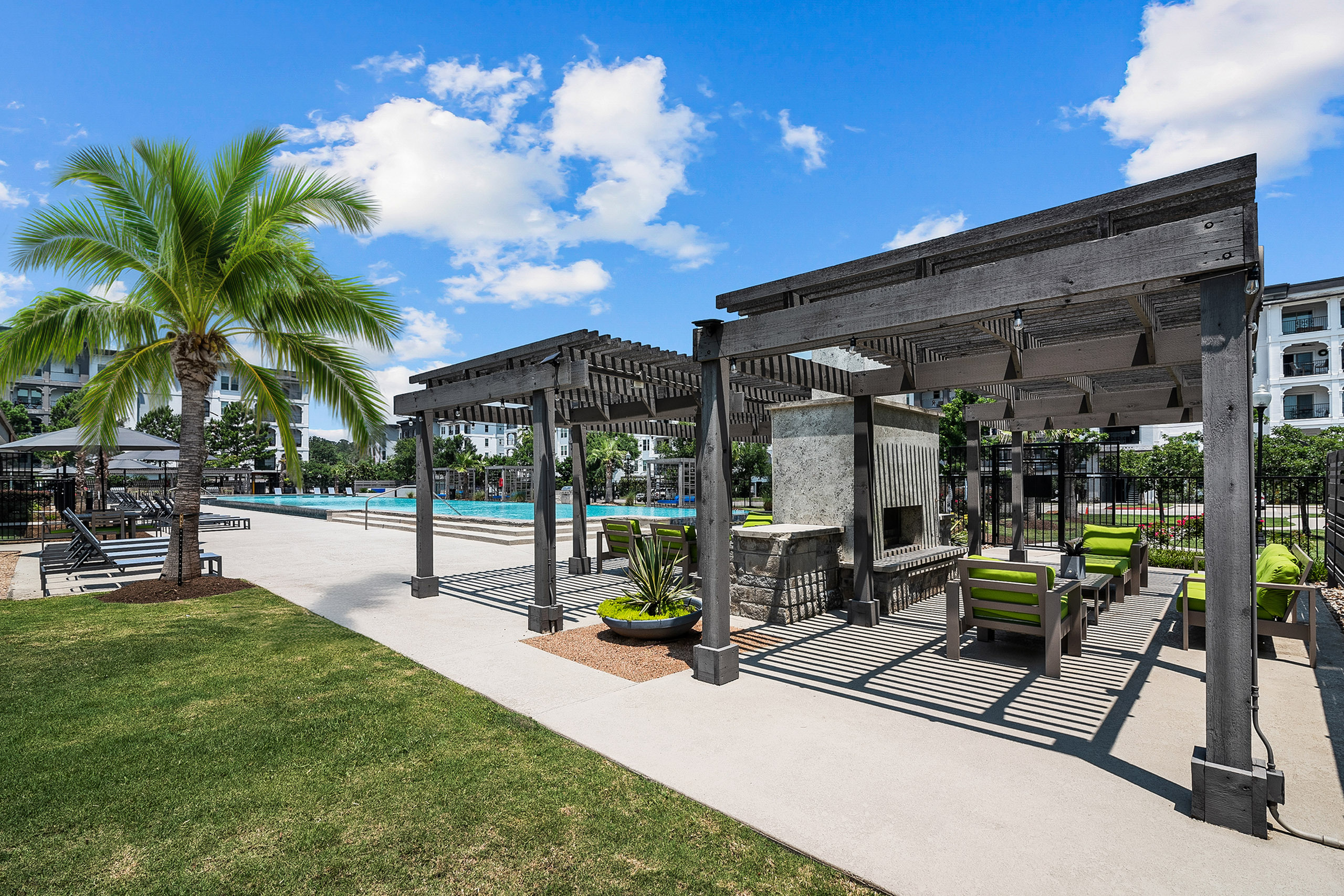 Luxurious outdoor patio featuring elegant pergolas, vibrant green seating, and a sparkling pool area surrounded by lush greenery and palm trees.