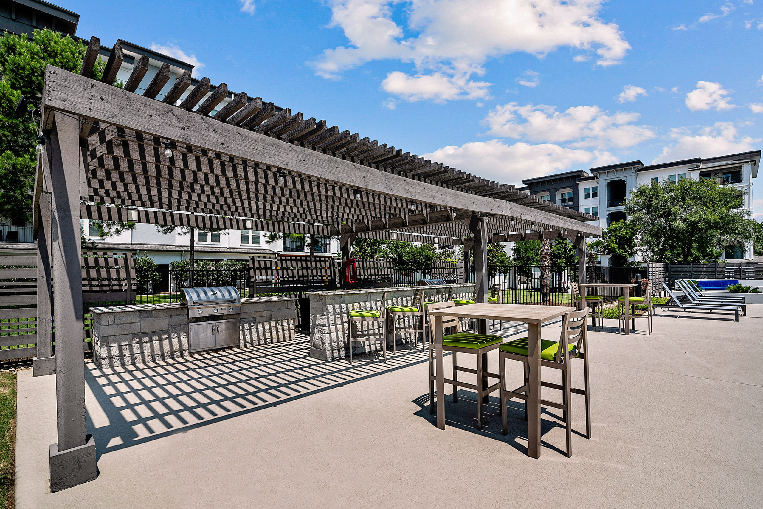 Spacious outdoor patio featuring a stylish pergola, modern barbecue grills, and comfortable seating in a vibrant apartment community.