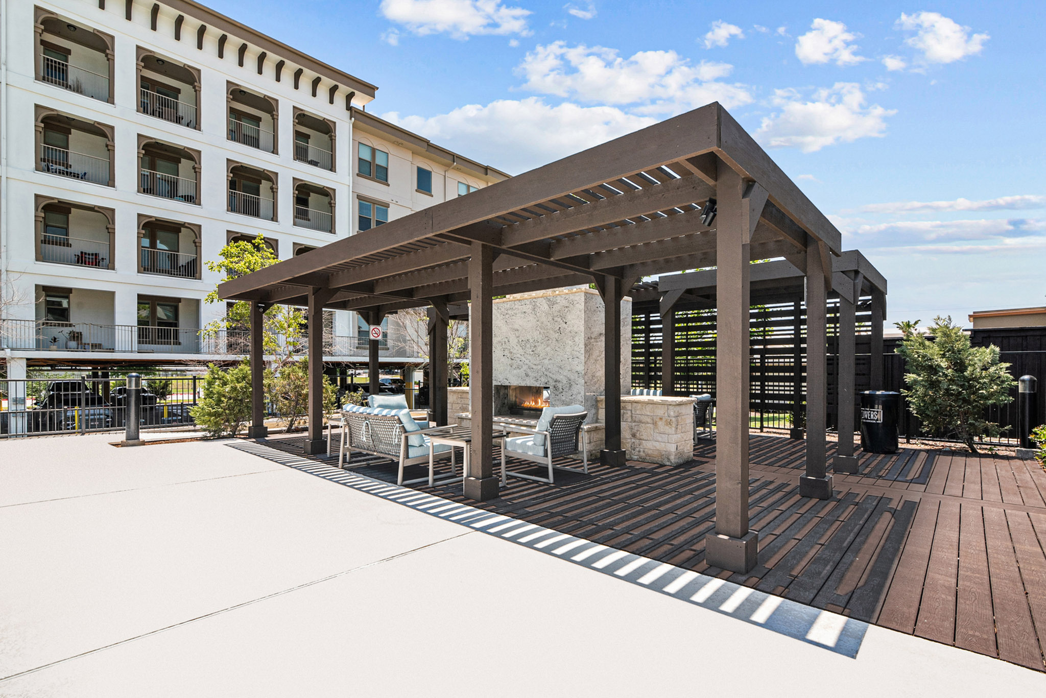 Modern outdoor seating area with elegant pergola and inviting fireplace, adjacent to a stylish apartment building.