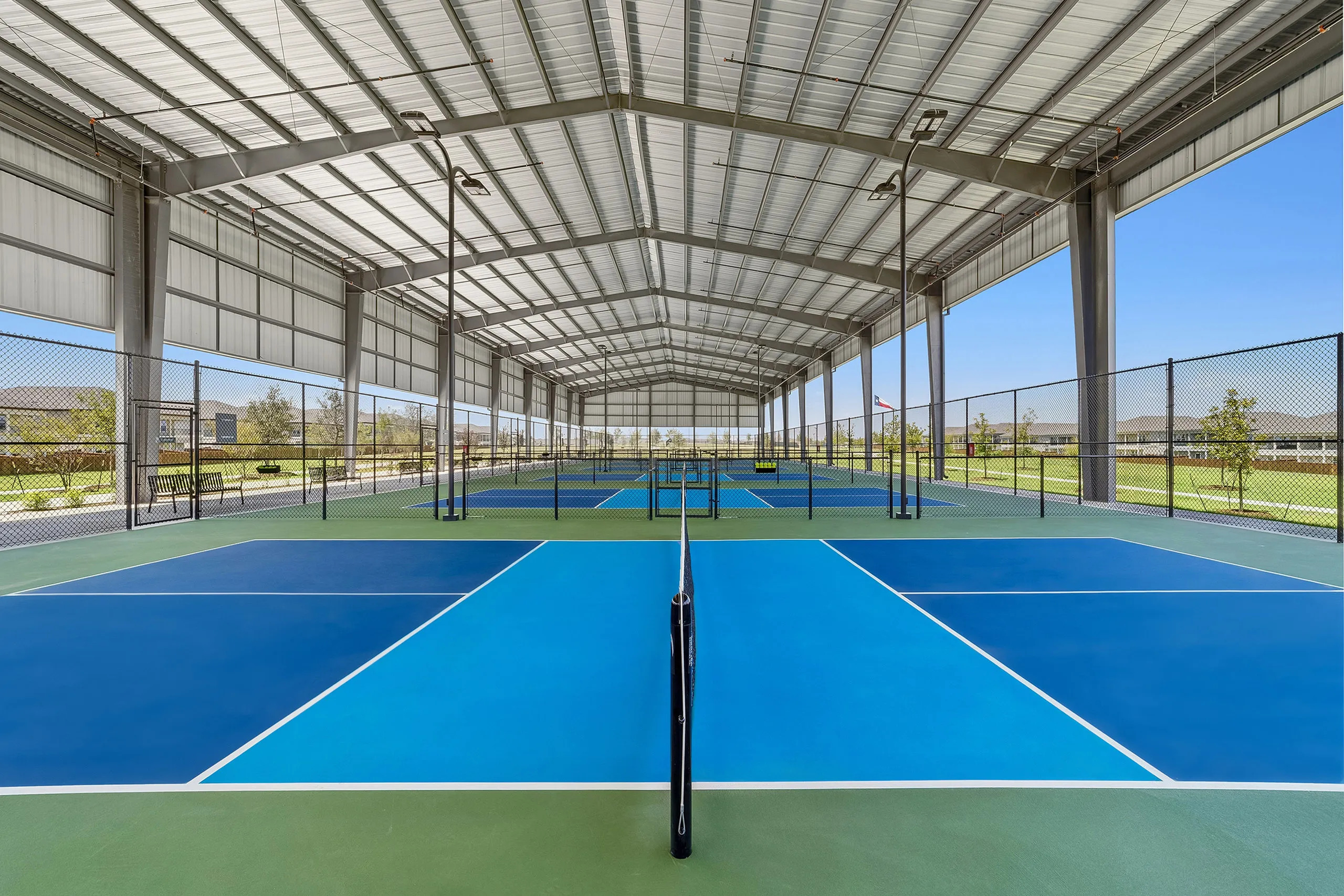 Eight covered and lighted Pickleball courts with vibrant blue surfaces and ample natural light, perfect for year-round play.