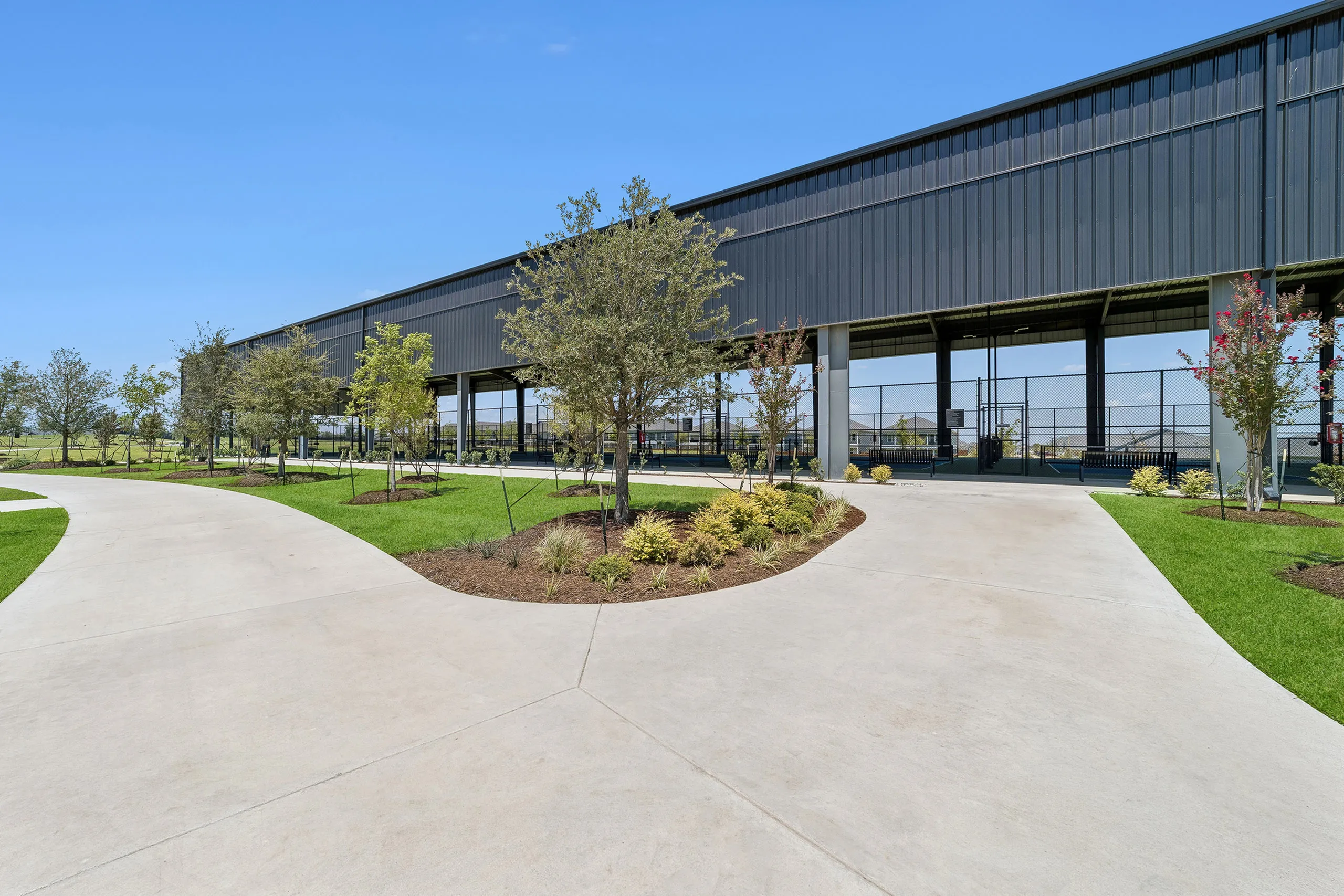 Eight covered and lighted Pickleball courts, lush landscaping, and winding pathways under a clear blue sky.