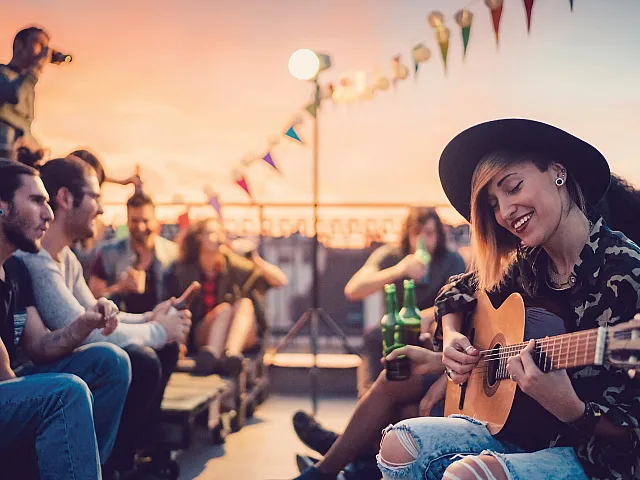 Vibrant rooftop party at sunset with friends enjoying music, drinks, and laughter under festive bunting.