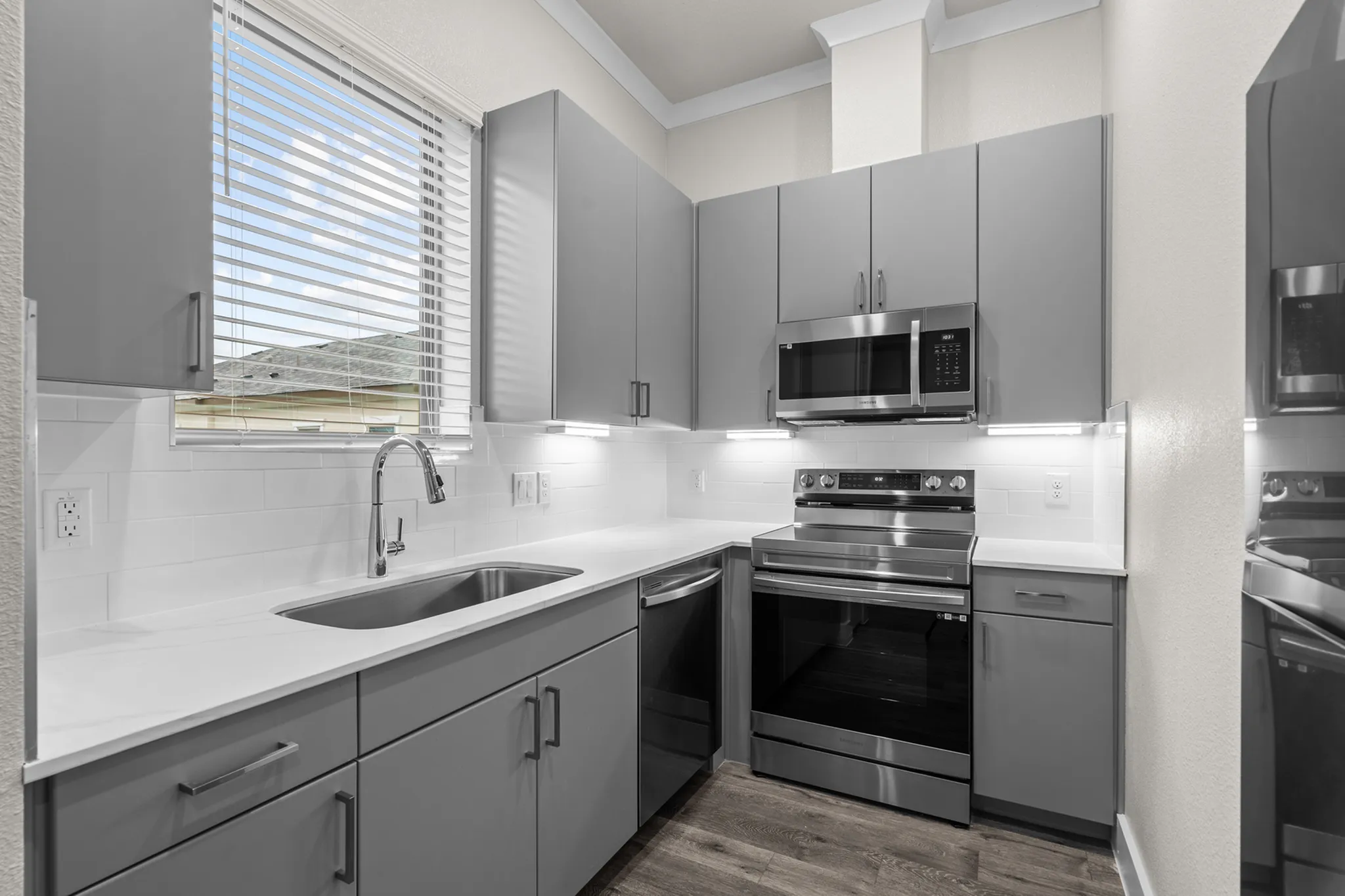Modern kitchen with sleek gray cabinetry, stainless steel appliances, and a bright window view | Apartments in Hutto, TX | Mansions Eight65