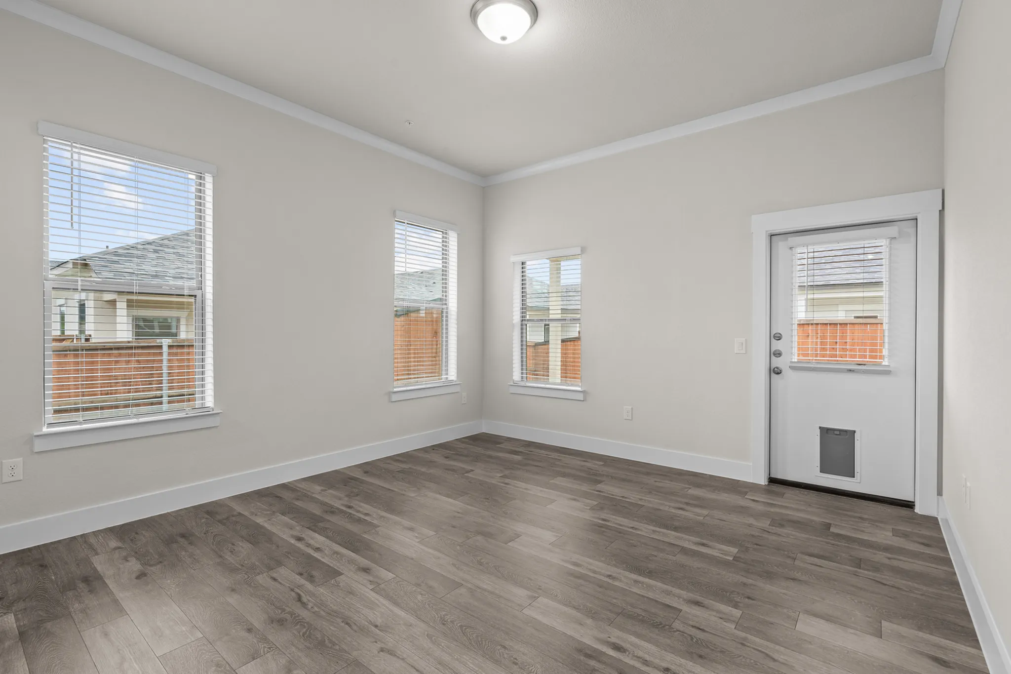 Bright, spacious bedroom with elegant wood flooring, large windows, and a door leading to a private outdoor space, offering plenty of natural light | Apartments in Hutto, TX | Mansions Eight65