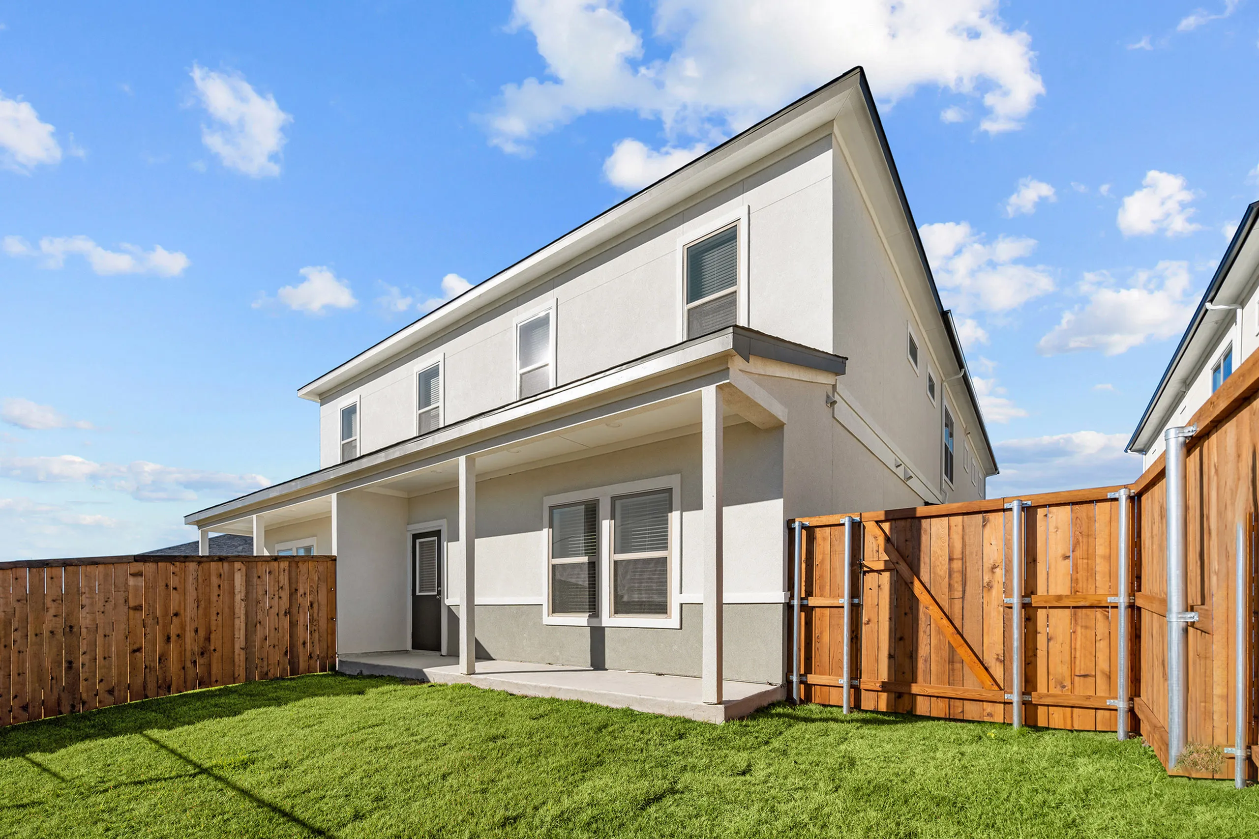 Charming modern apartment exterior with a spacious green backyard and wooden fencing under a clear blue sky.