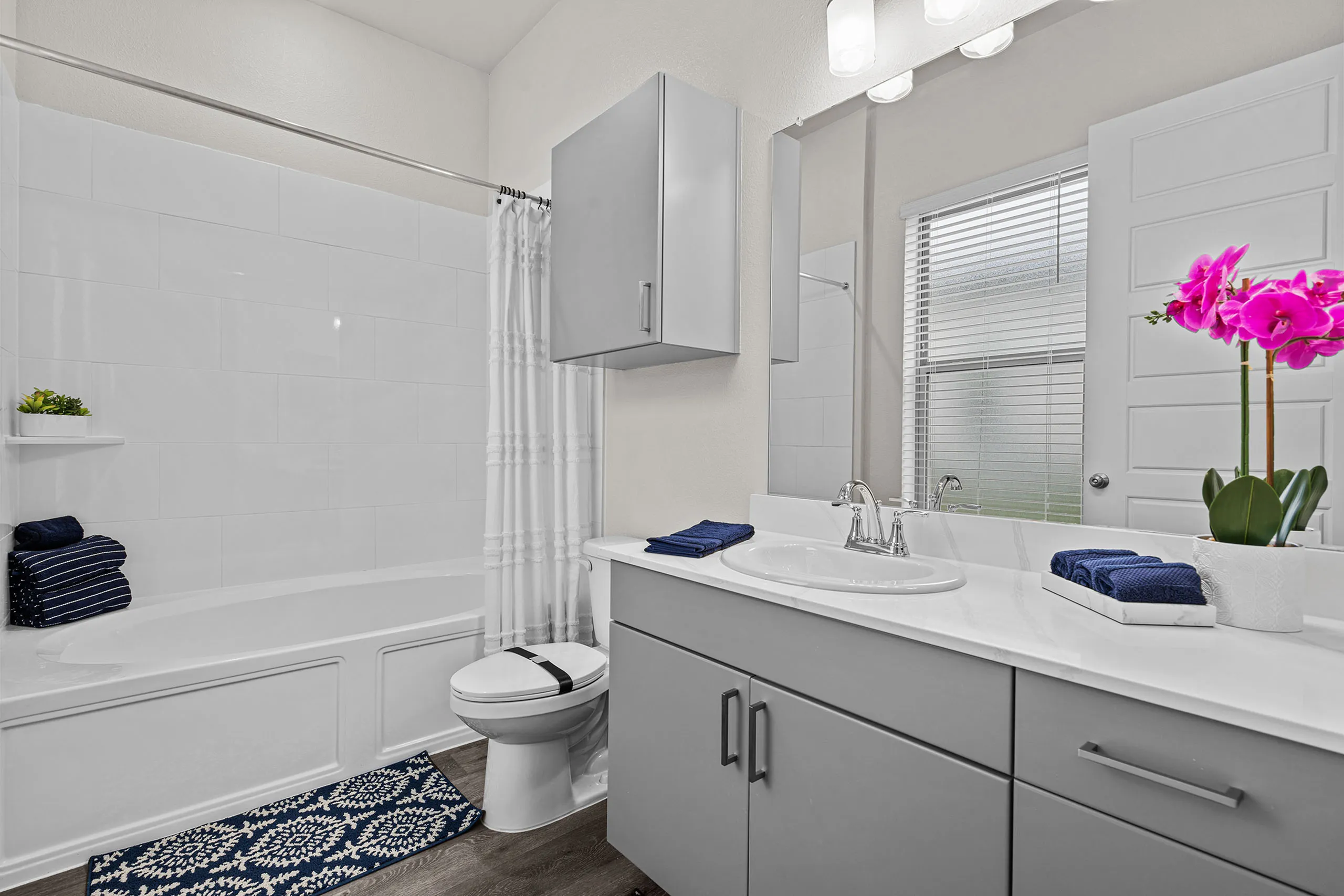 Modern bathroom design with elegant gray cabinets, bright lighting, and a luxurious bathtub, accented with vibrant orchid flowers.