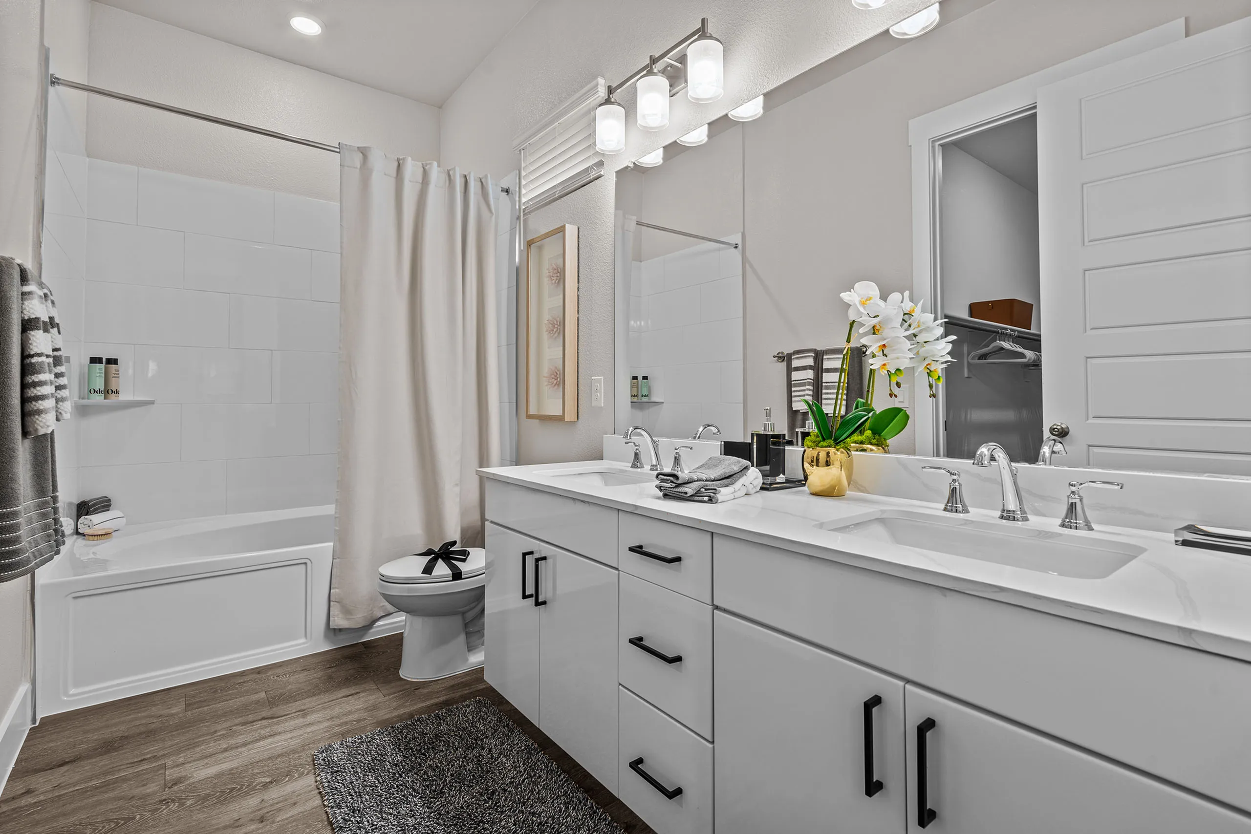 Elegant bathroom featuring a double vanity with sleek white cabinets, modern fixtures, and a relaxing bathtub. Accentuated by bright lighting and stylish decor.