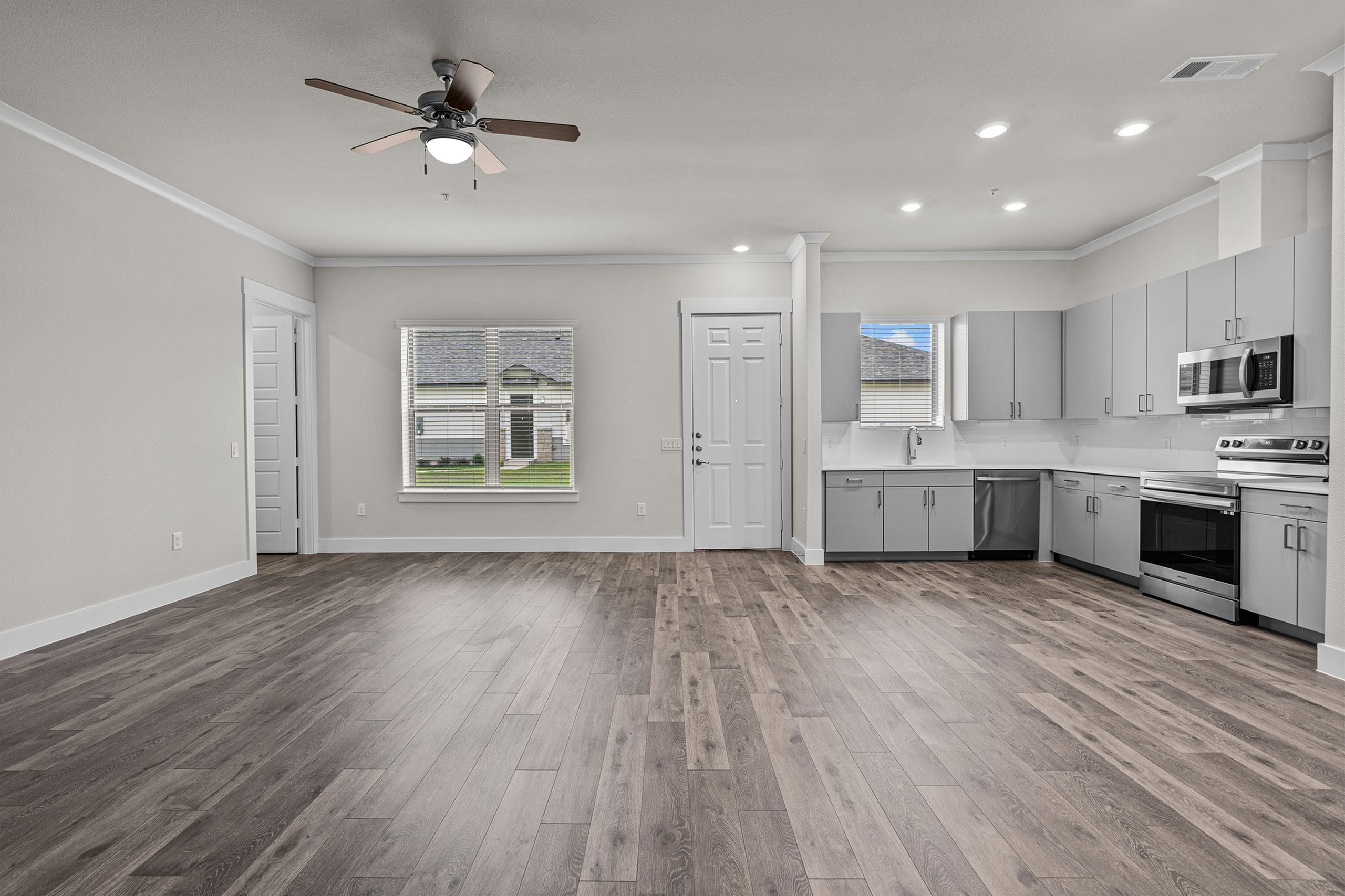 Spacious open-plan living area with modern kitchen featuring sleek cabinetry, stainless steel appliances, and elegant wood flooring, complemented by ample natural light from large windows.
