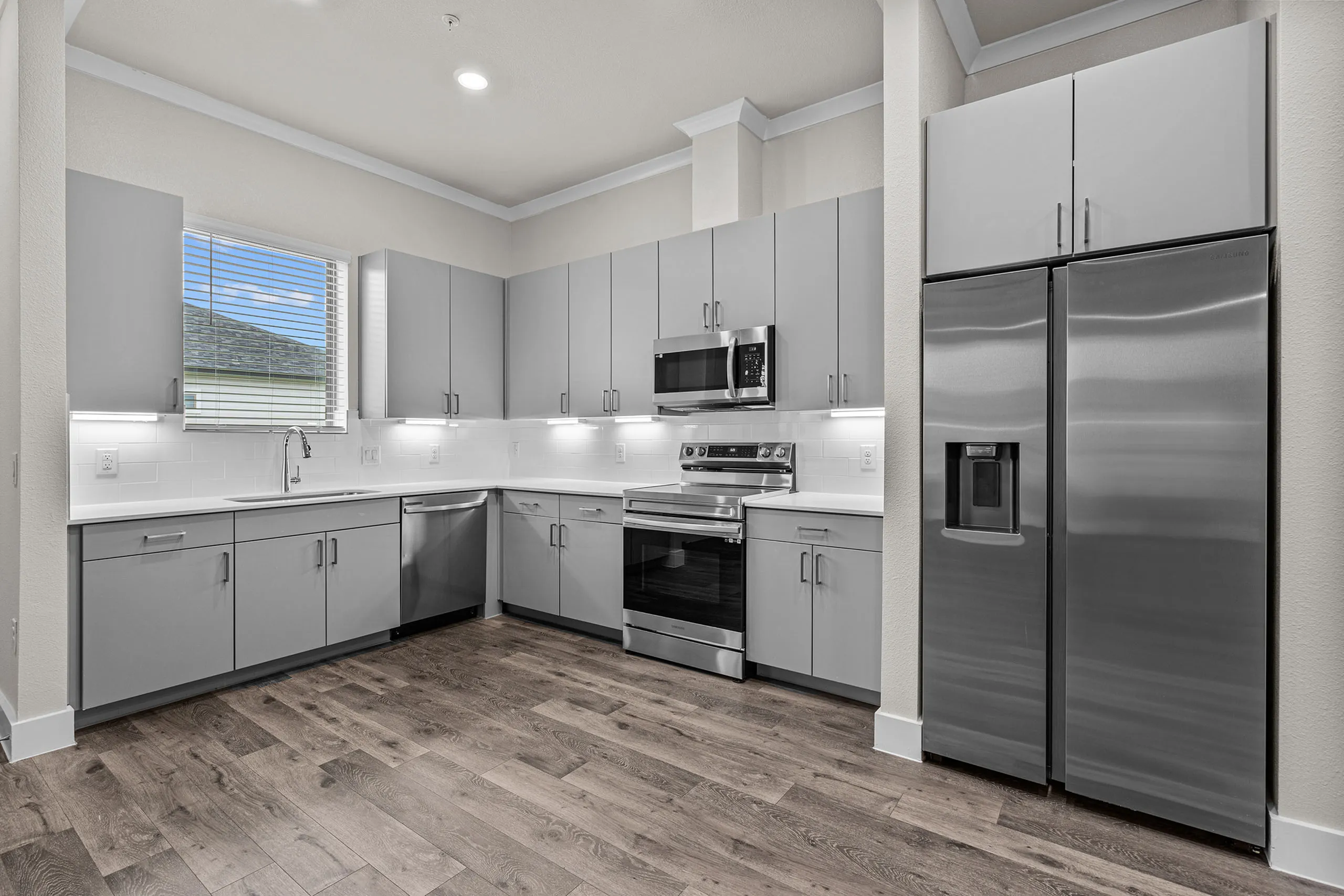 Contemporary kitchen with sleek gray cabinets, modern stainless steel appliances, and elegant wood flooring.