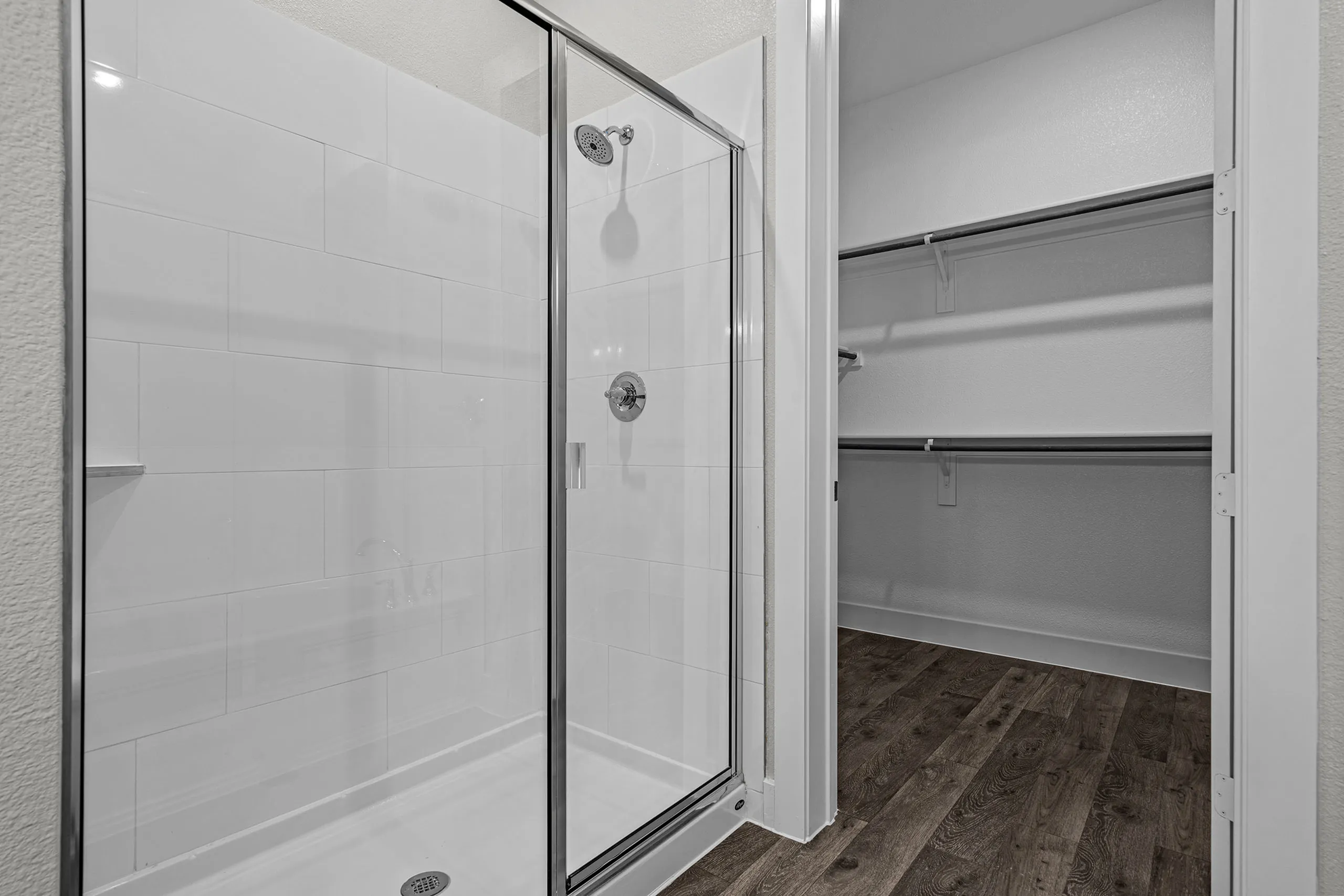 Modern bathroom view featuring a sleek glass shower and a spacious walk-in closet with wooden flooring.