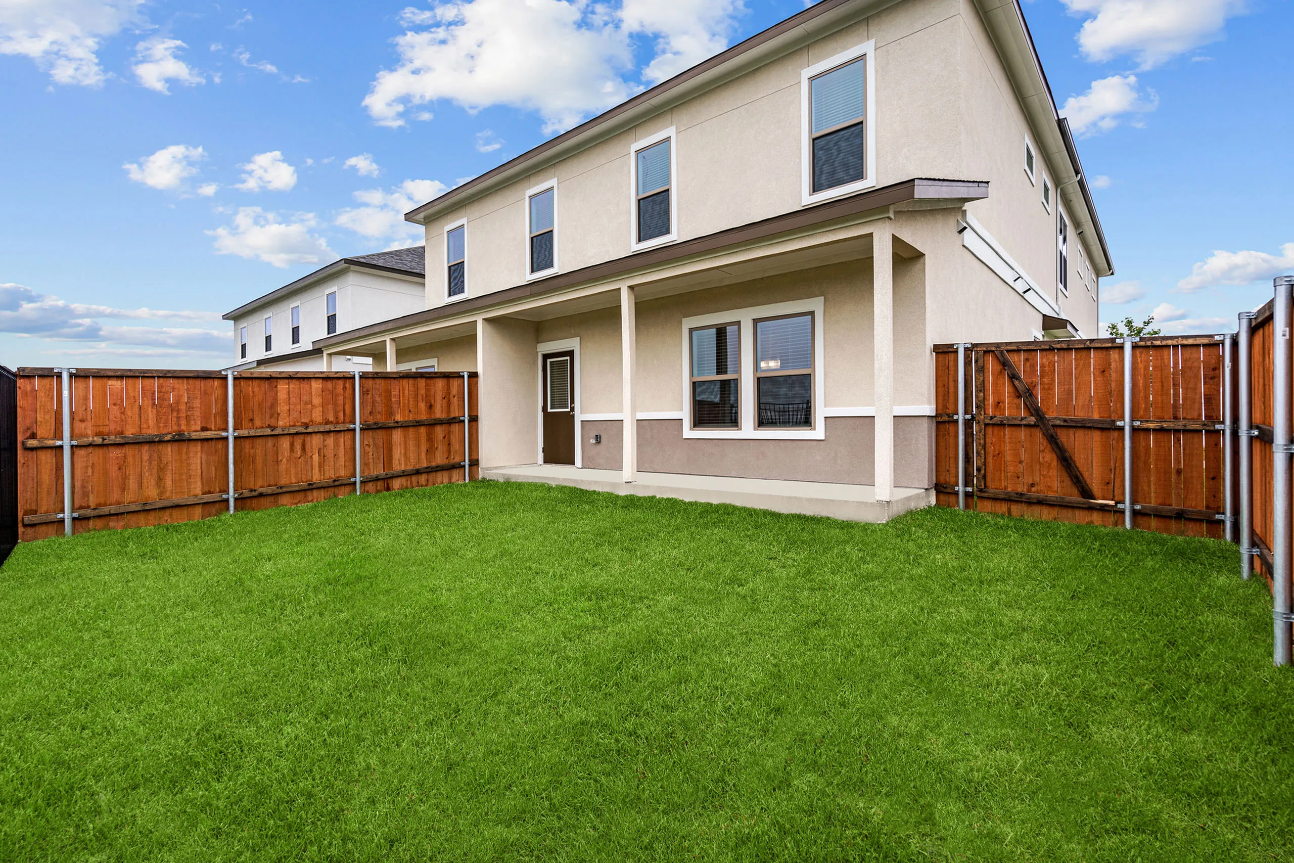 Charming backyard view of a modern two-story home with a well-maintained lawn and privacy fence under a clear blue sky.