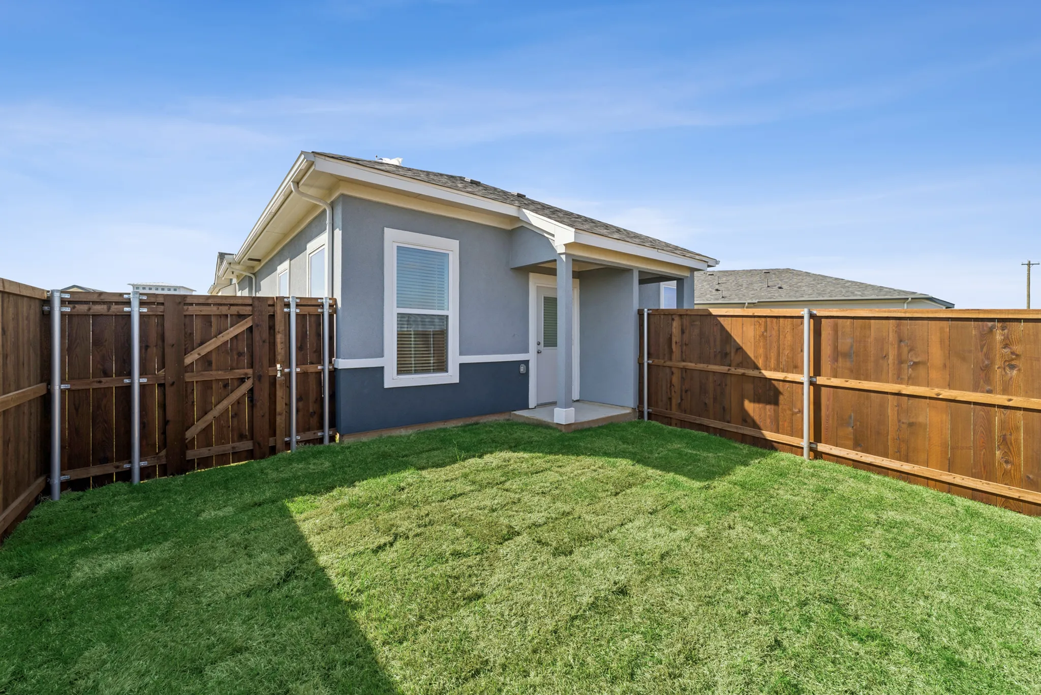 Charming backyard view of a modern home with a wooden fence, vibrant green lawn, and blue sky.